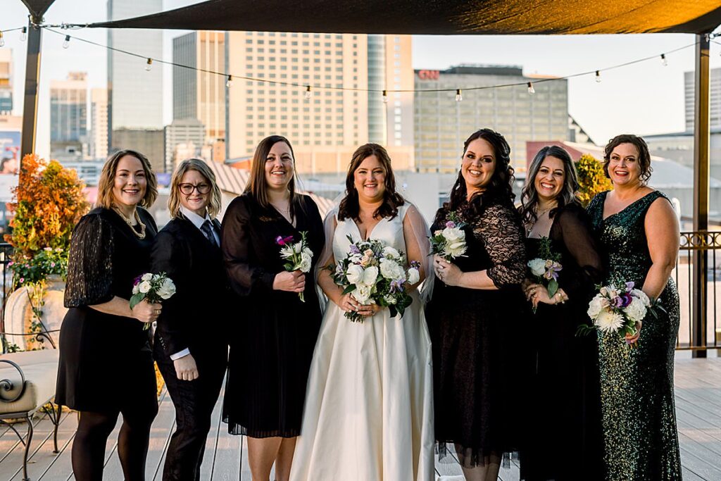 A bride stands on a balcony with her wedding party in black dresses 