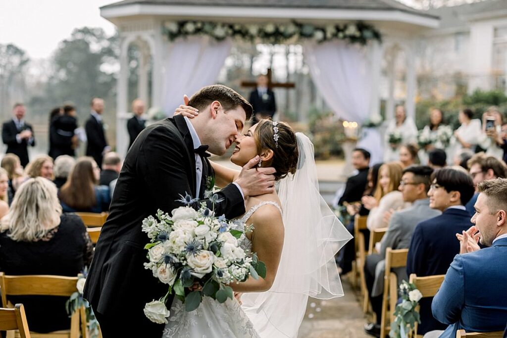 Newlyweds kiss as their guests celebrate after their ceremony Little River Farms, wedding venue in Milton Georgia