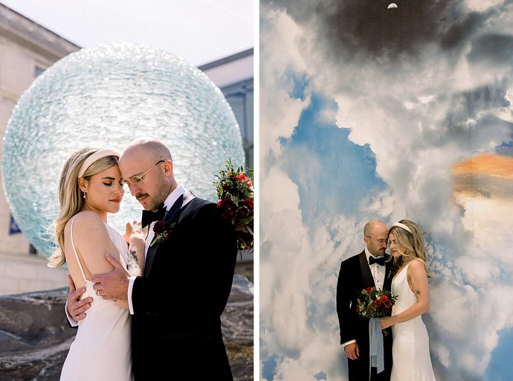 Newlyweds embrace in front of a large glass globe and sky mural
