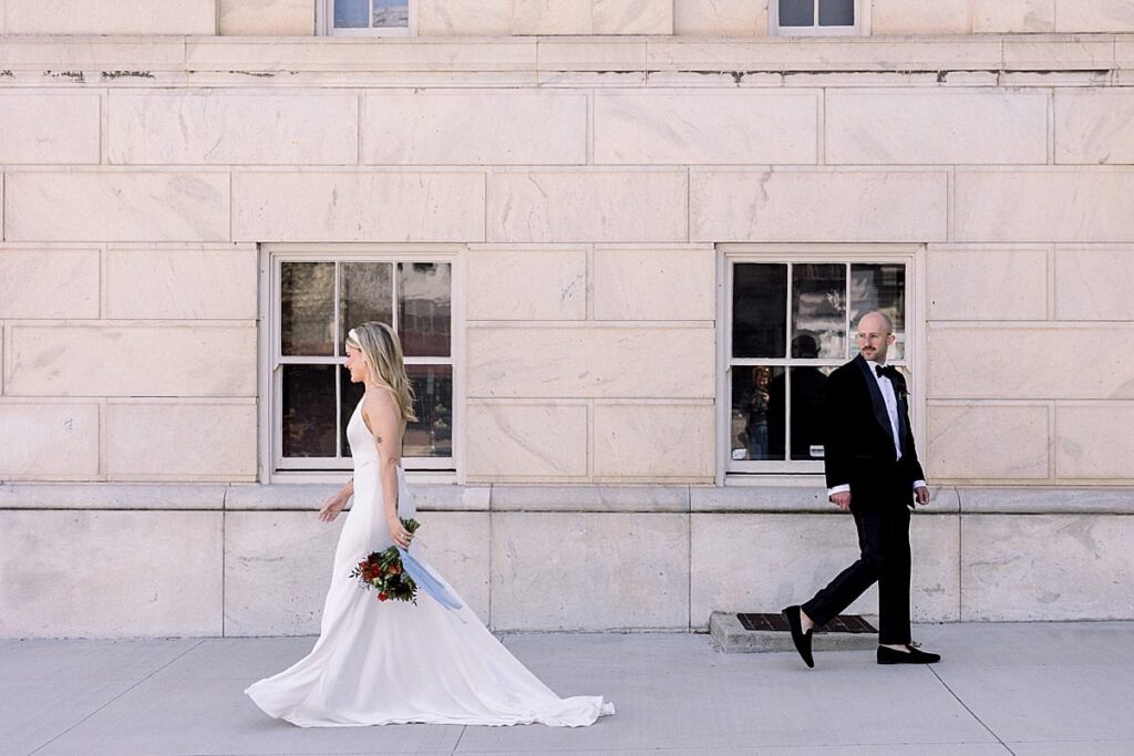 Newlyweds walk past each other outside a stone building