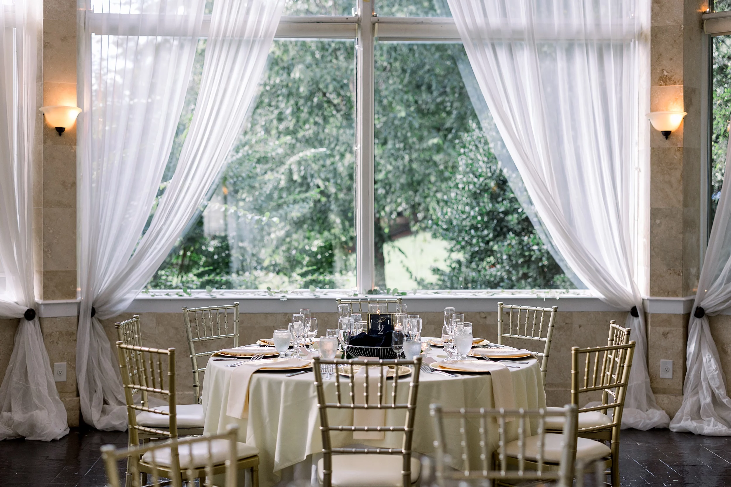 Table setting under a window with gold chairs and neutral linens