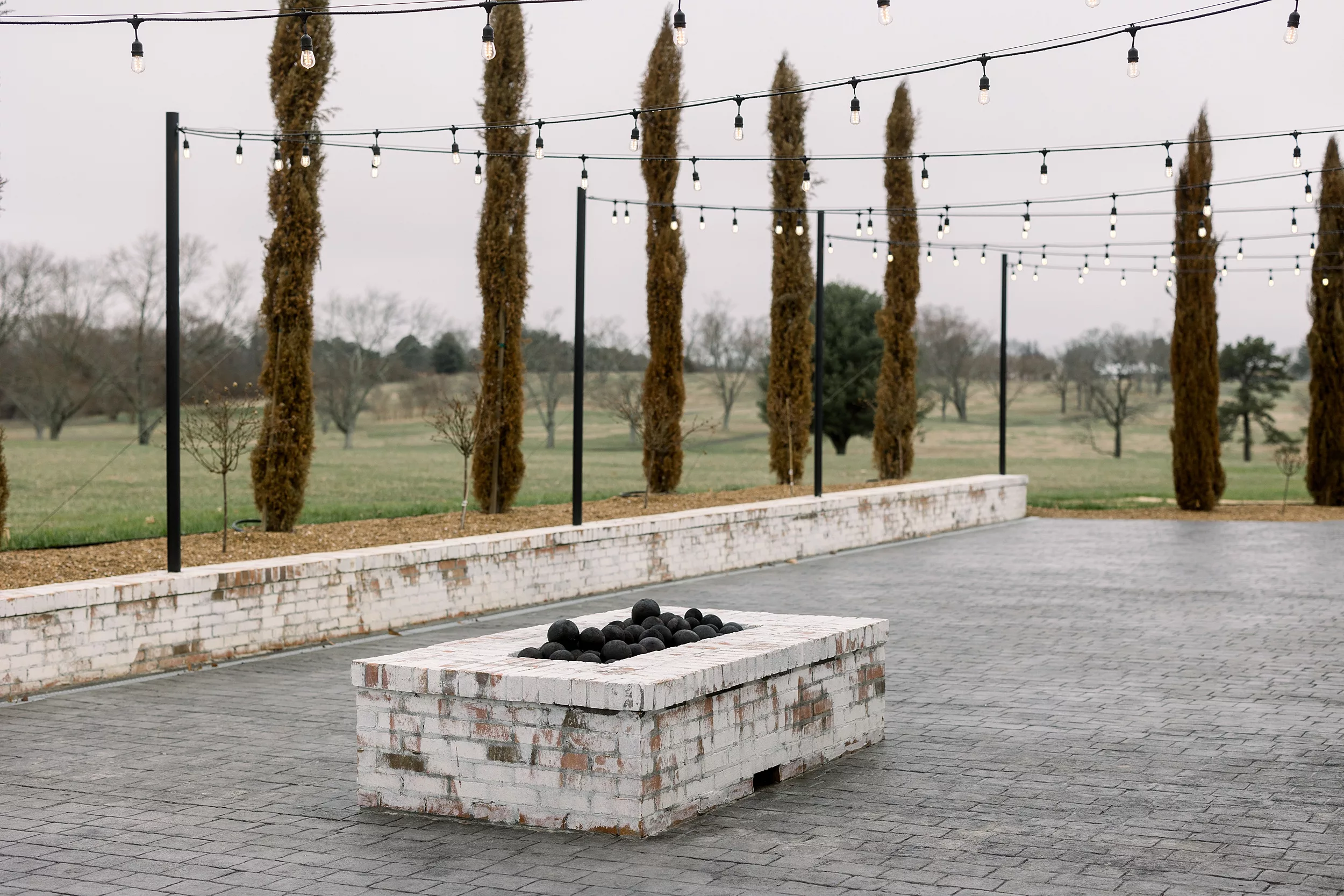 Stone patio with market lights, white wash brick retaining wall and fire pit at blackberry ridge wedding venue