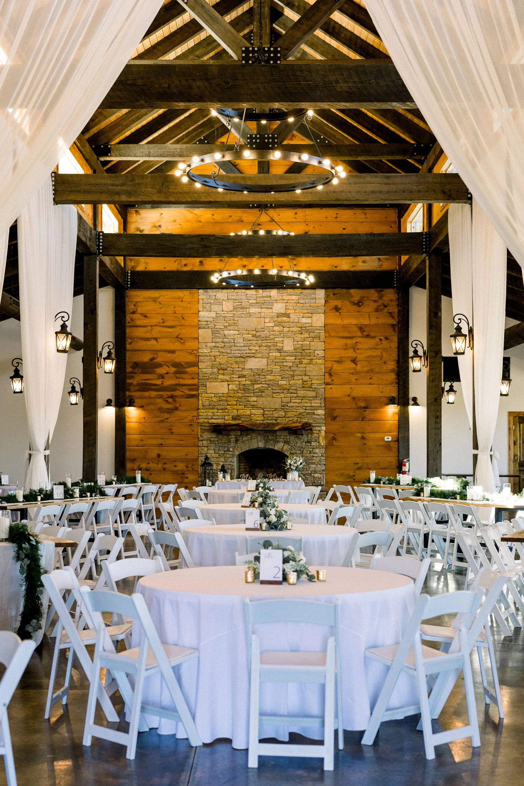 Details of a Barn wedding reception setup with white linen and chairs and a large stone fireplace at a Blue Mountain Vineyards Wedding