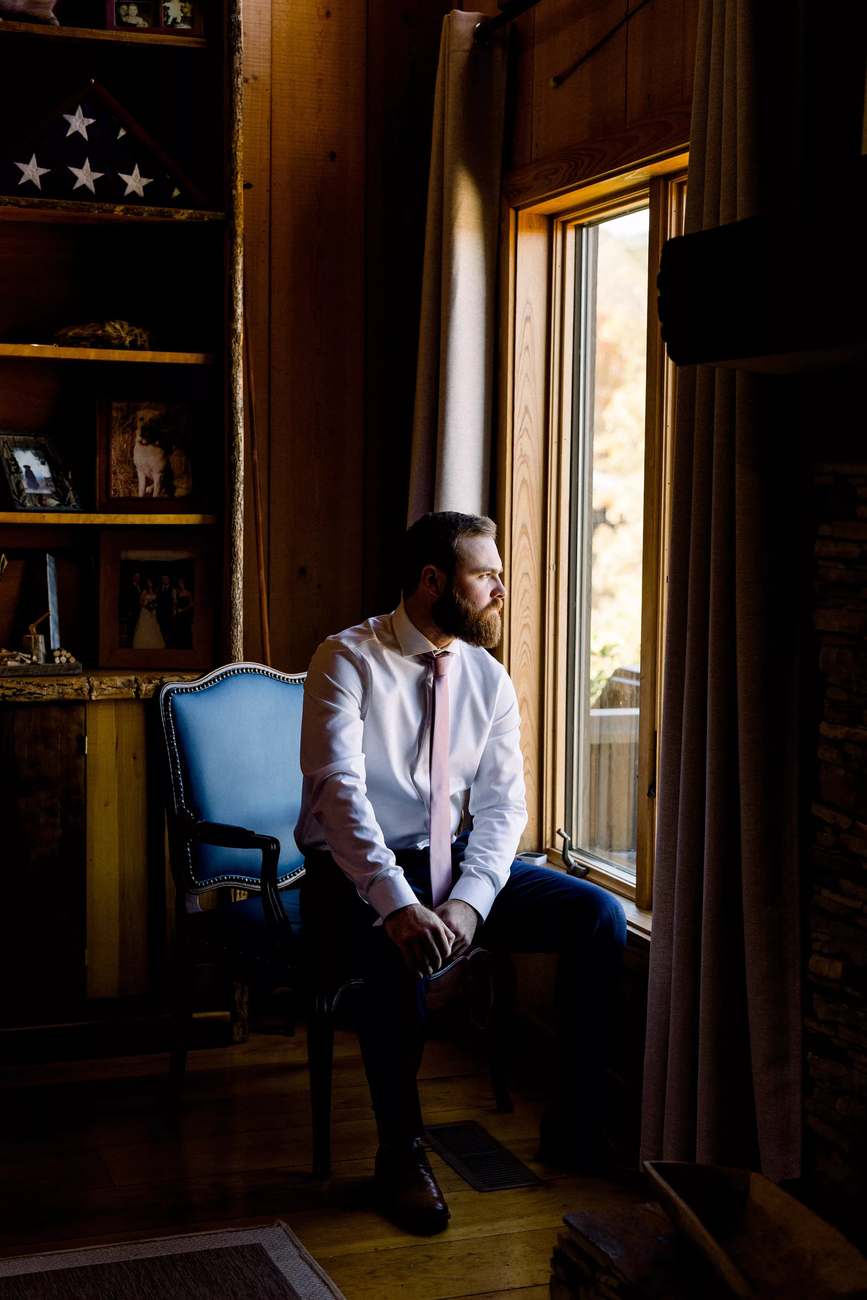 A man in a white shirt and pink tie sits in an antique chair looking out a window at Blue Mountain Vineyards Wedding
