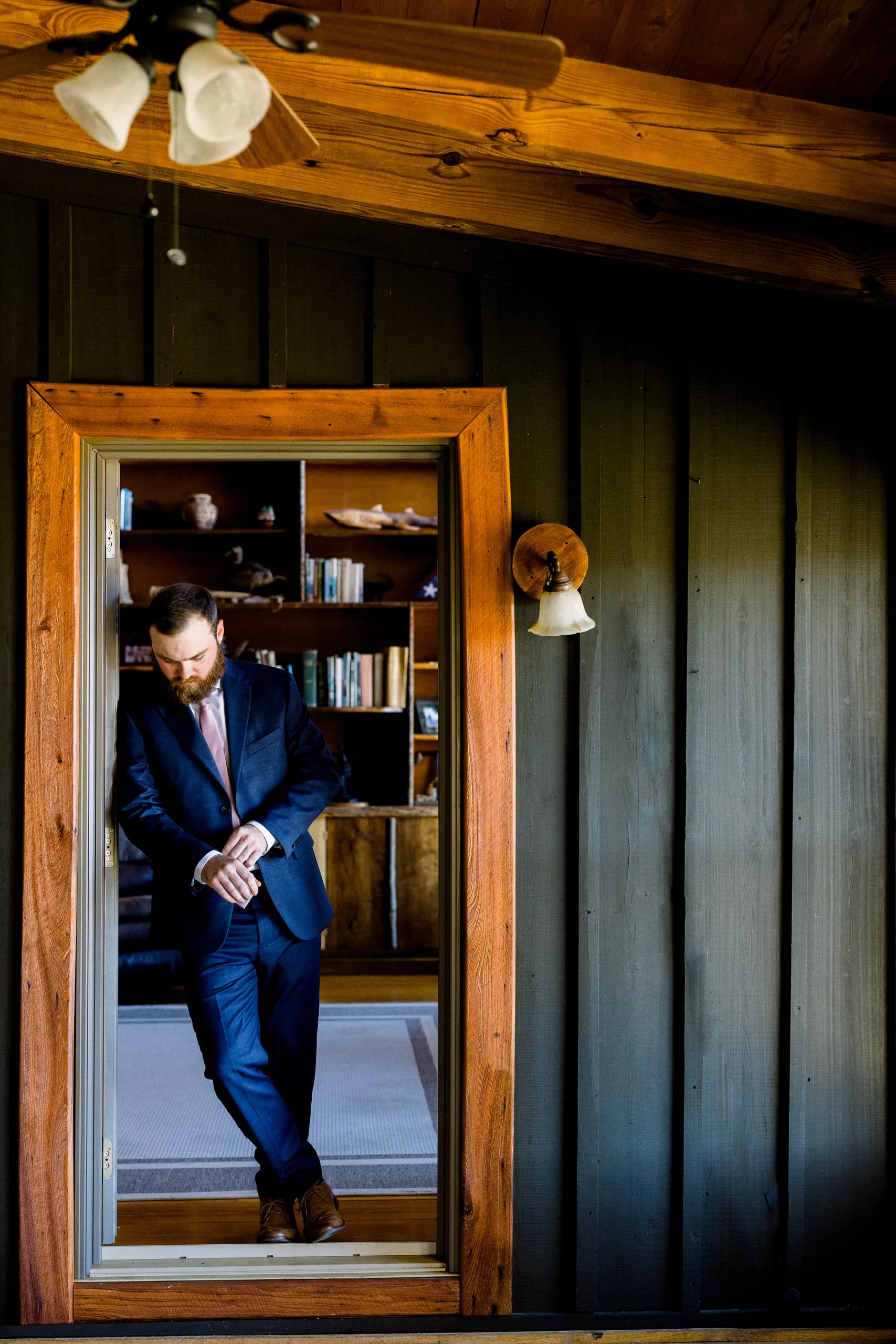 A groom in a blue suit stands in a door adjusting his sleeves at Blue Mountain Vineyards Wedding