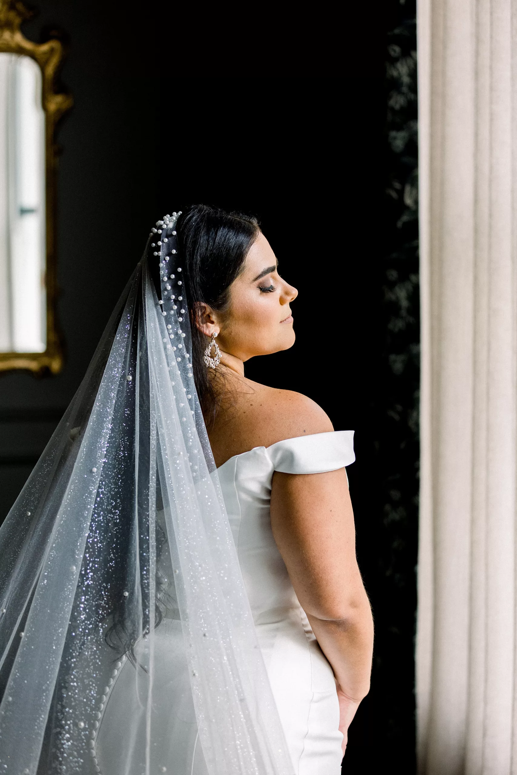 A bride stands in a window in her white dress and long veil