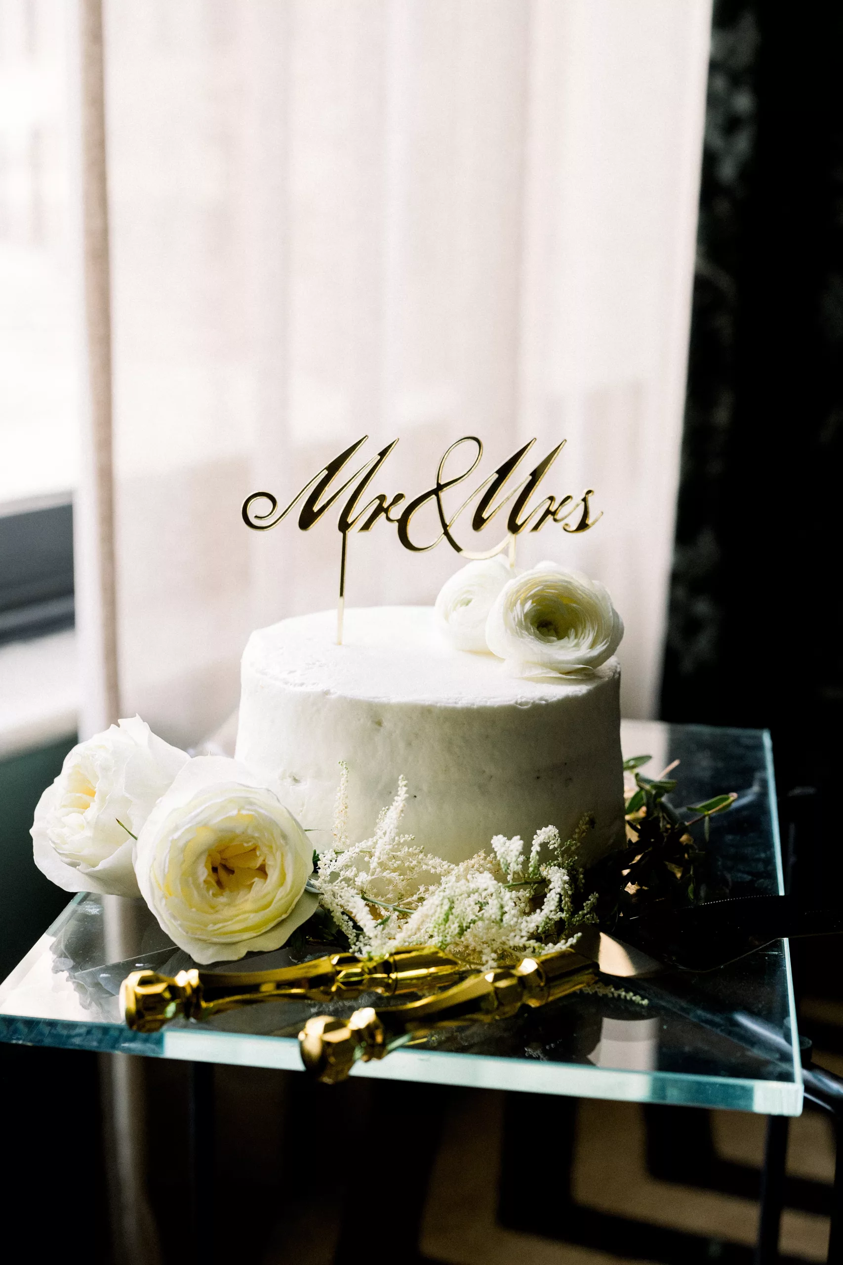 Details of a single tier wedding cake with white roses and gold utensils 