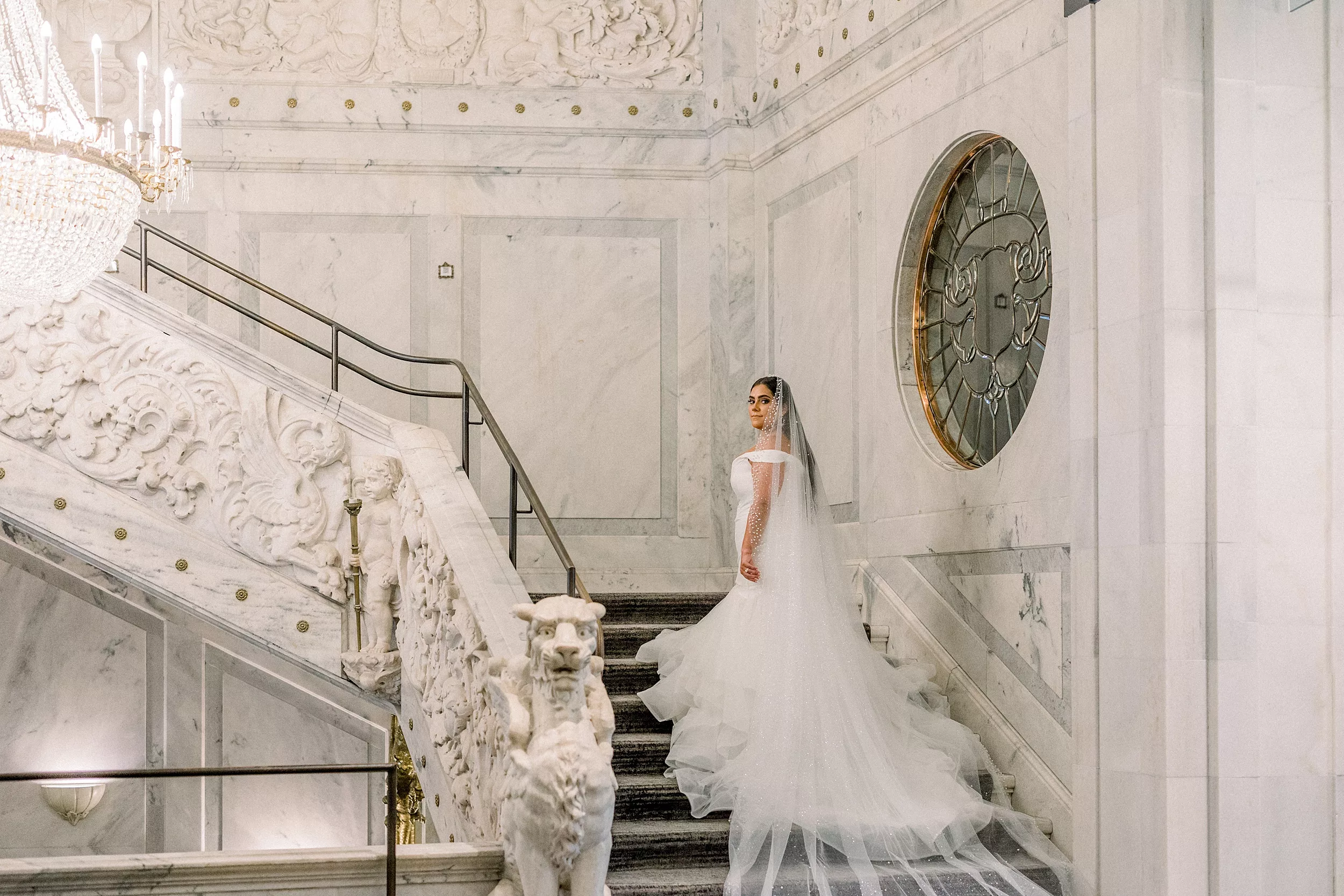 A bride looks over her shoulder while walking up a marble staircase with at Candler Hotel Atlanta wedding