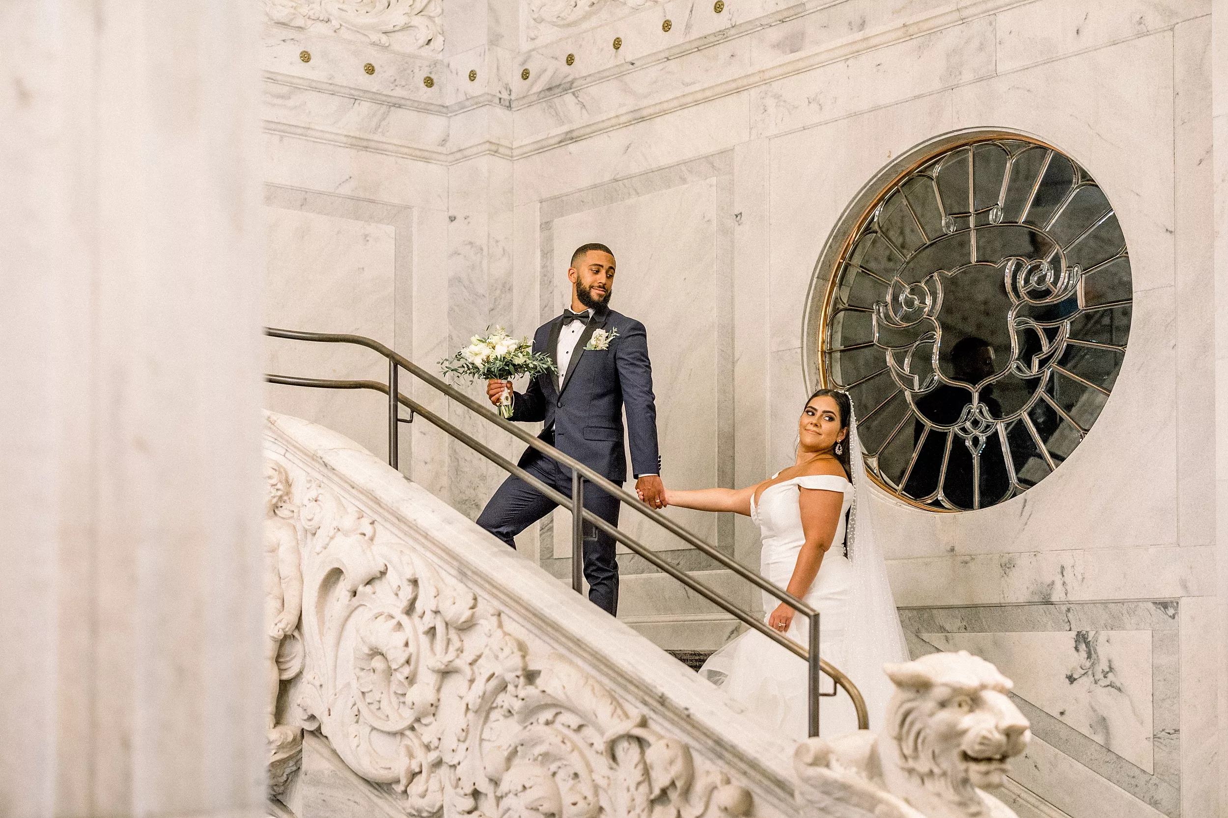 A groom leads his bride up a marble staircase at a Candler Hotel Atlanta wedding