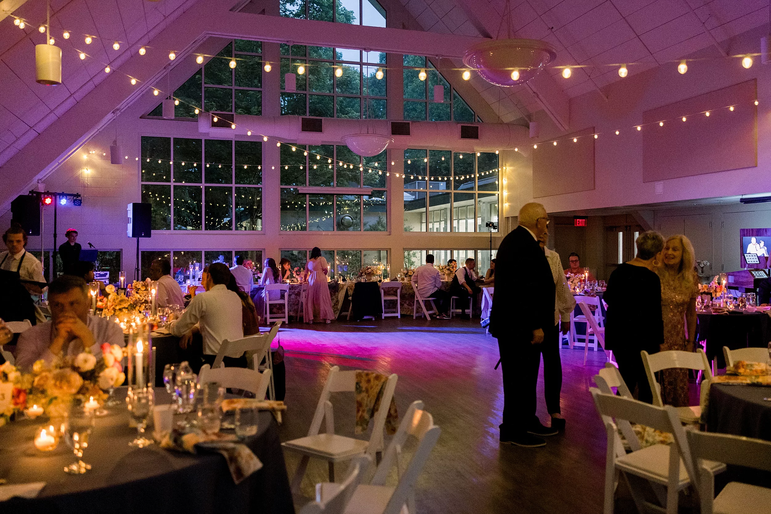 A wedding reception with a large wall of windows, market and DJ lights and people talking at a Cator Woolford Gardens Elopement