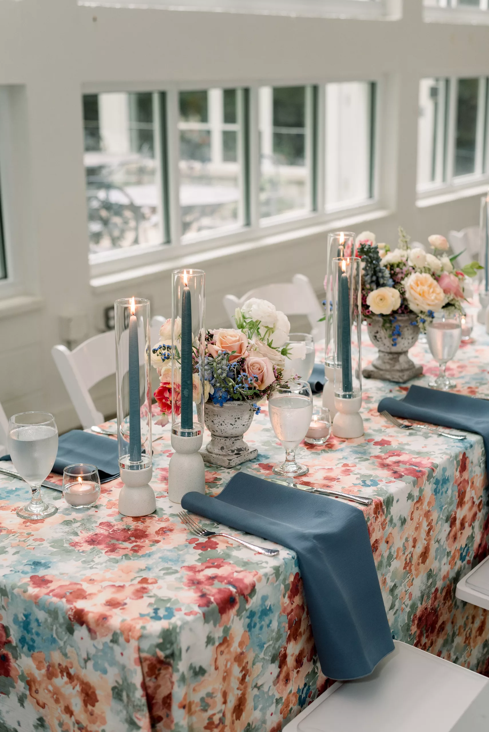Details of a table setting with floral linen tablecloth and matching blue napkins and candles