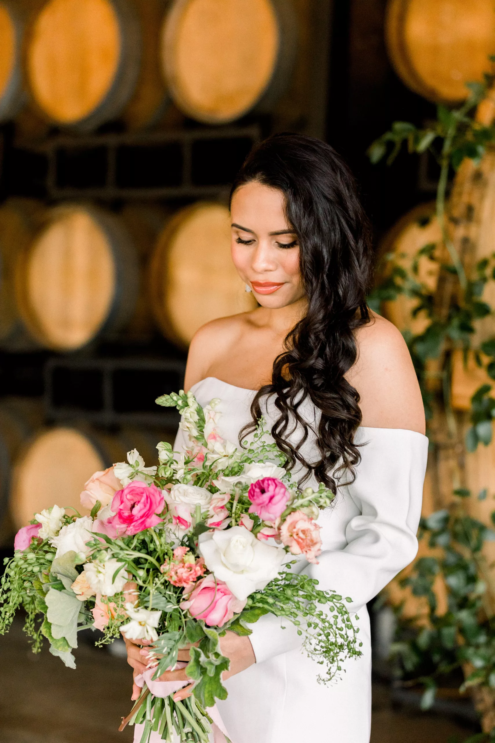 A bride gazes down at her bouquet in her hands while standing in a room full of wine barrels at a Chateau Elan Wedding