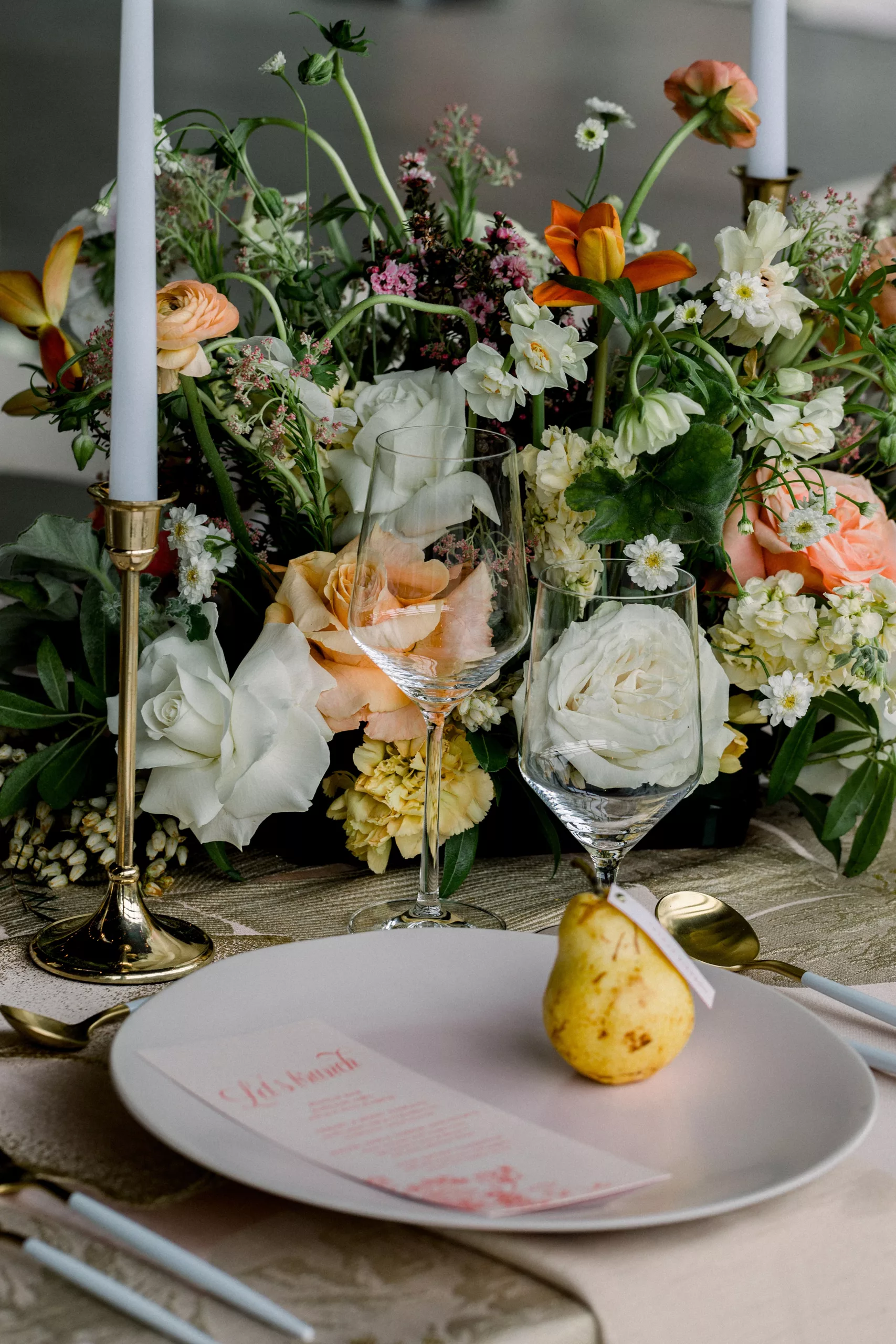 Details of a table setting with colorful florals and white candles on a wood table