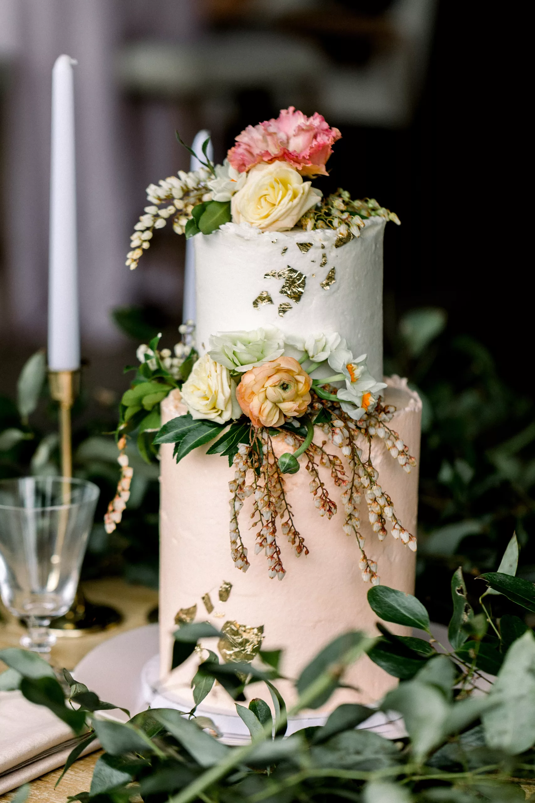 Details of a two tier wedding cake with florals and gold leaf