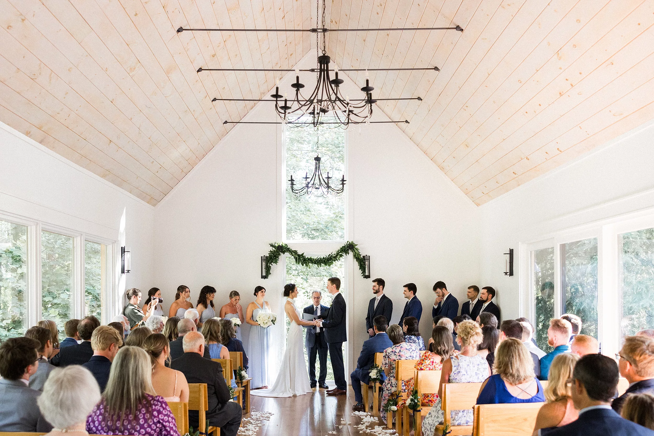 Newlyweds stand in front of the officiant holding hands during their ceremony full of guests at a Juliette Chapel Wedding