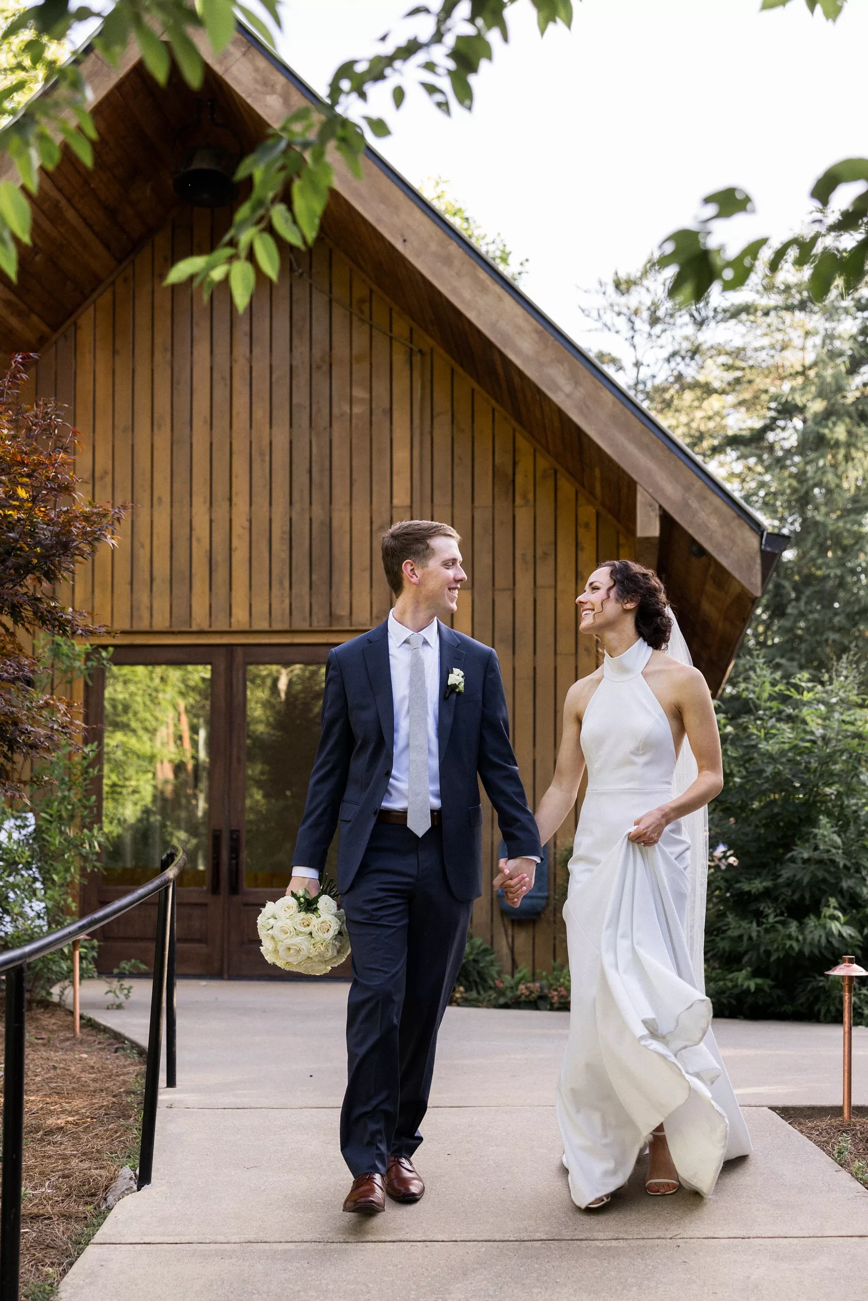 Newlyweds walk down a garden sidewalk holding hands in front of a cabin at a Juliette Chapel Wedding