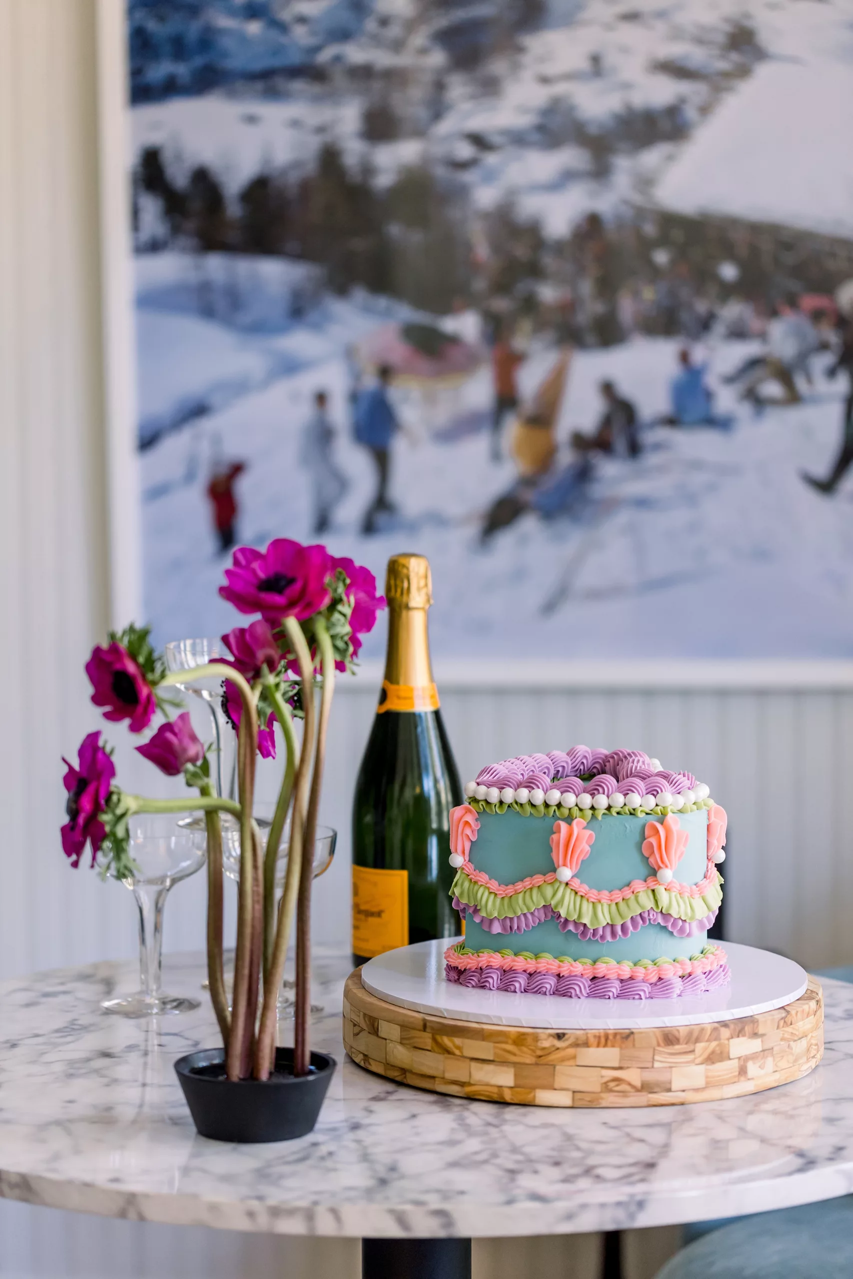 Details of a small colorful wedding cake with a bottle of champagne on a marble table