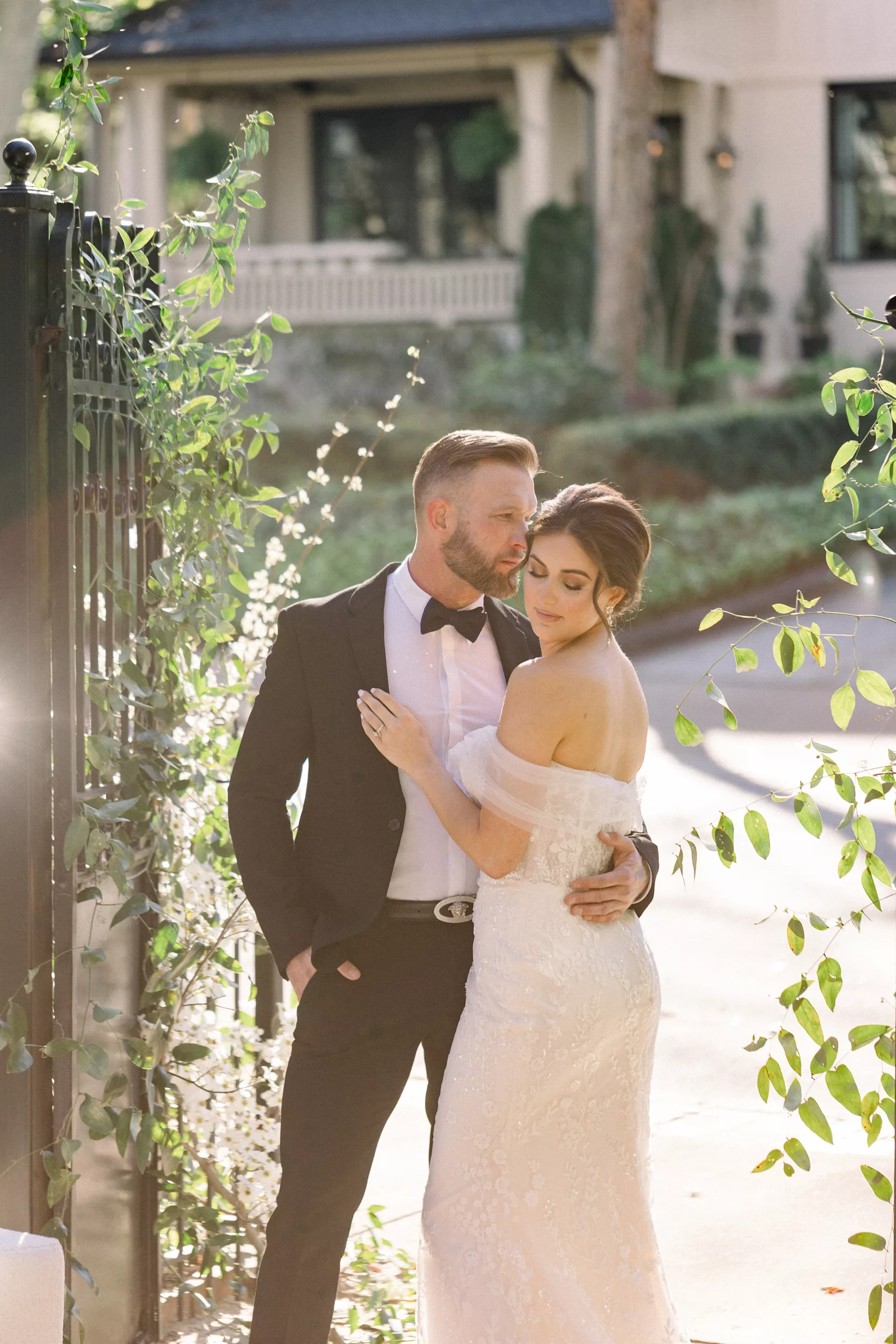 Newlyweds embrace each other while standing by a large iron gate covered in vines Wedding Photography Timeline