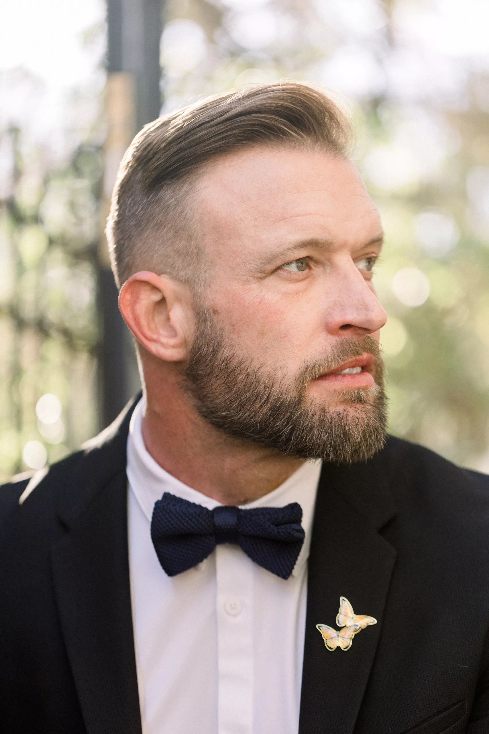 Details of a groom looking over his shoulder with a butterfly pin on his lapel Wedding Photography Timeline