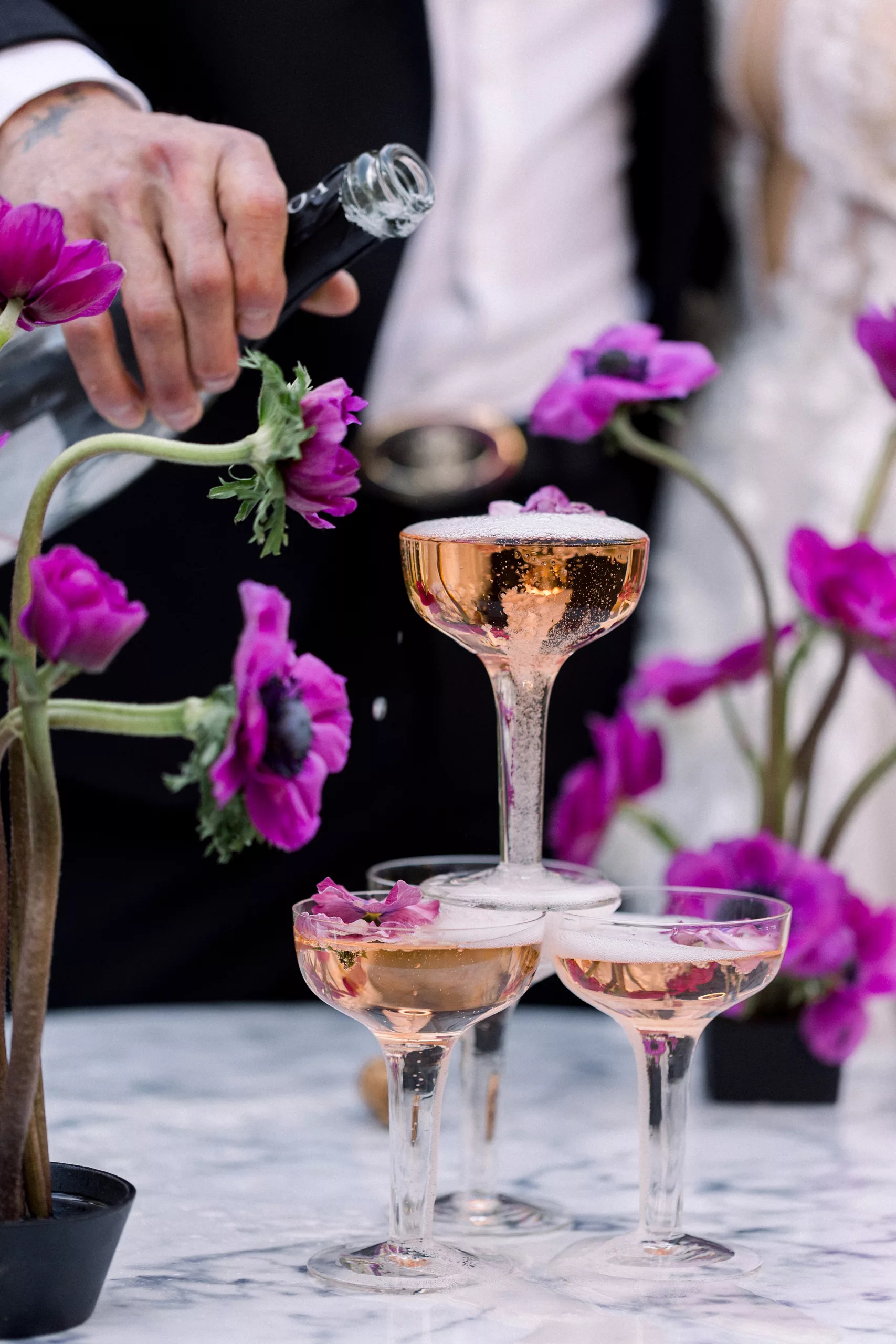 Details of a groom pouring champagne around purple flowers