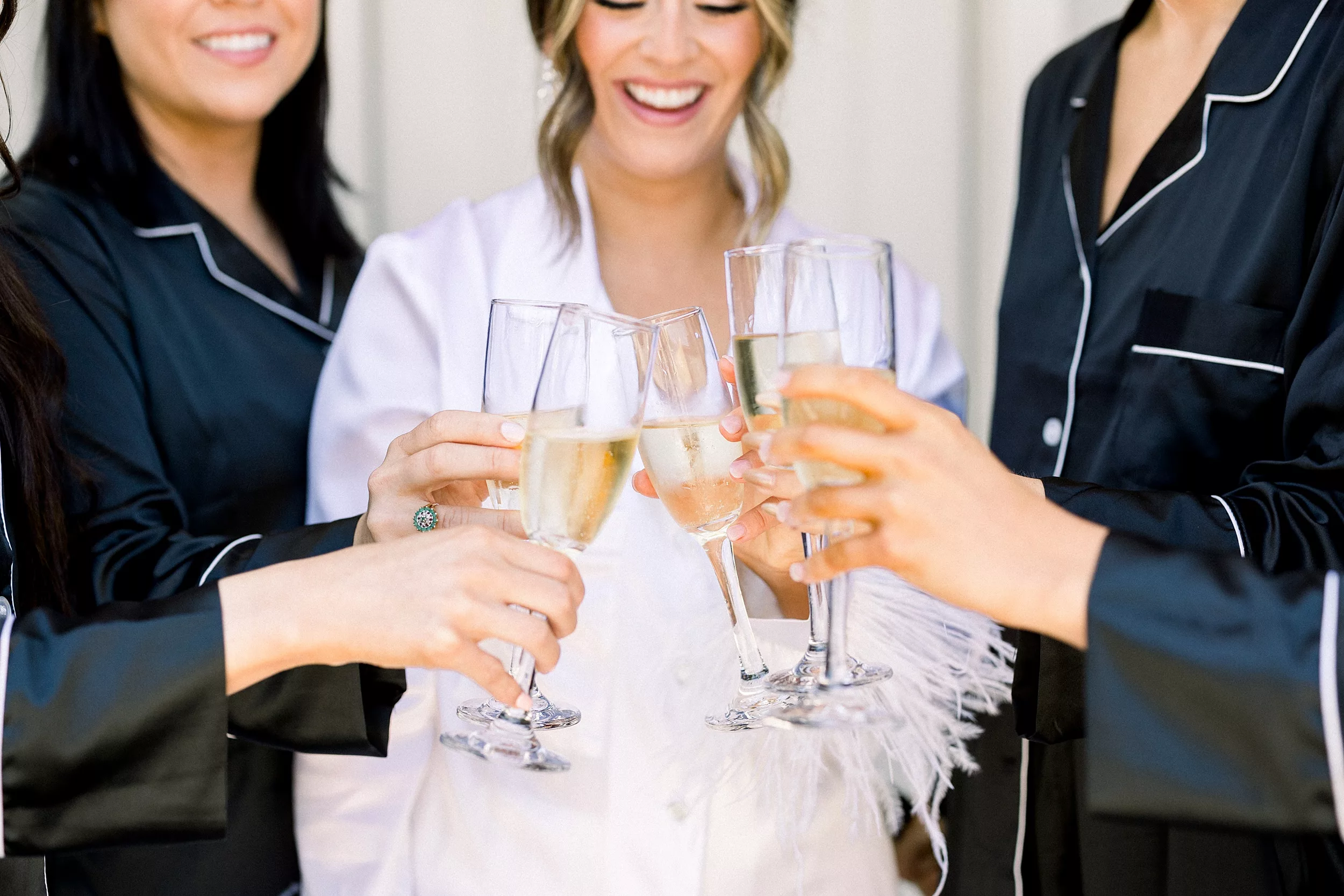 A bride toasts champagne with her bridesmaids in black and white pajamas wedding planner vs coordinator