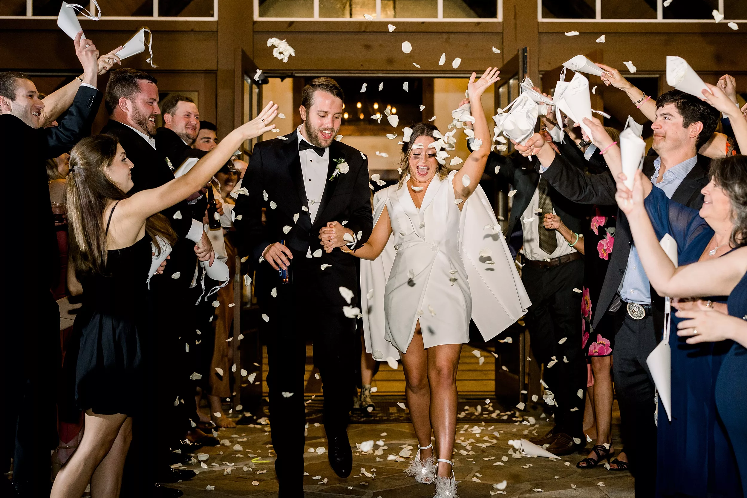Newlyweds exit their wedding while their guests throw white rose petals over them 