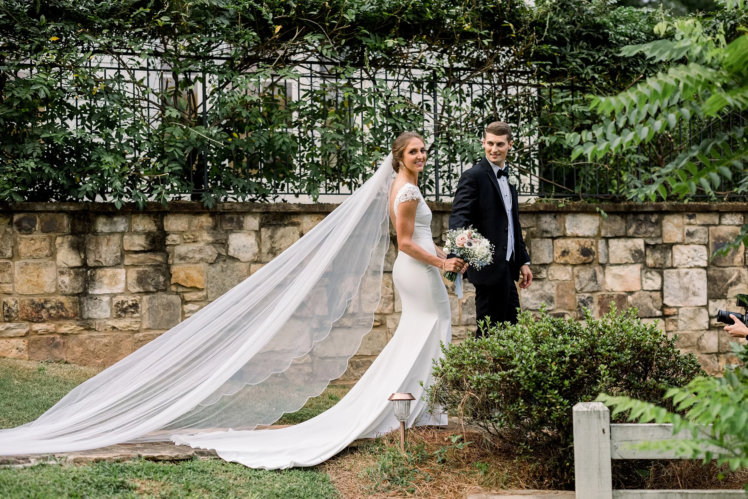 Newlyweds walk holding hands along a stone wall in a garden wedding planner vs coordinator