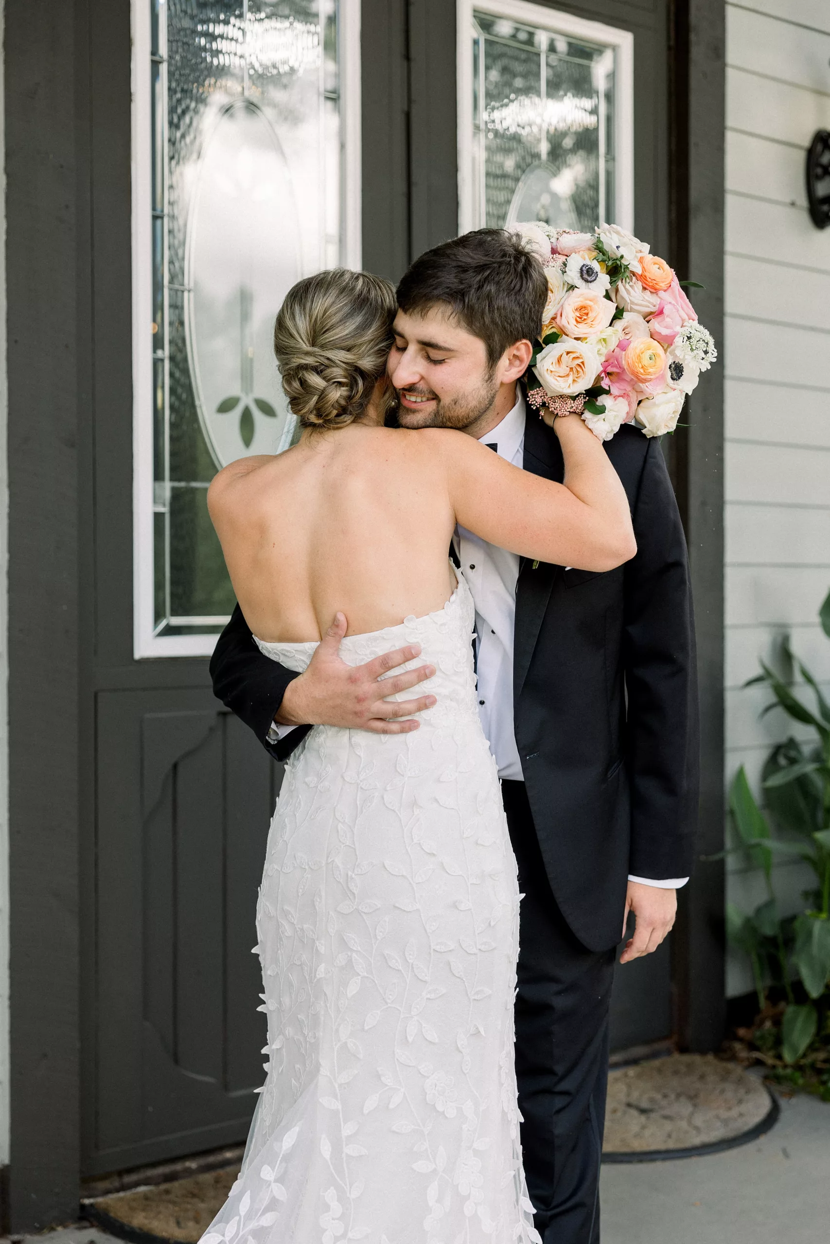 A groom hugs his bride on a porch as he sees her dress for the first time