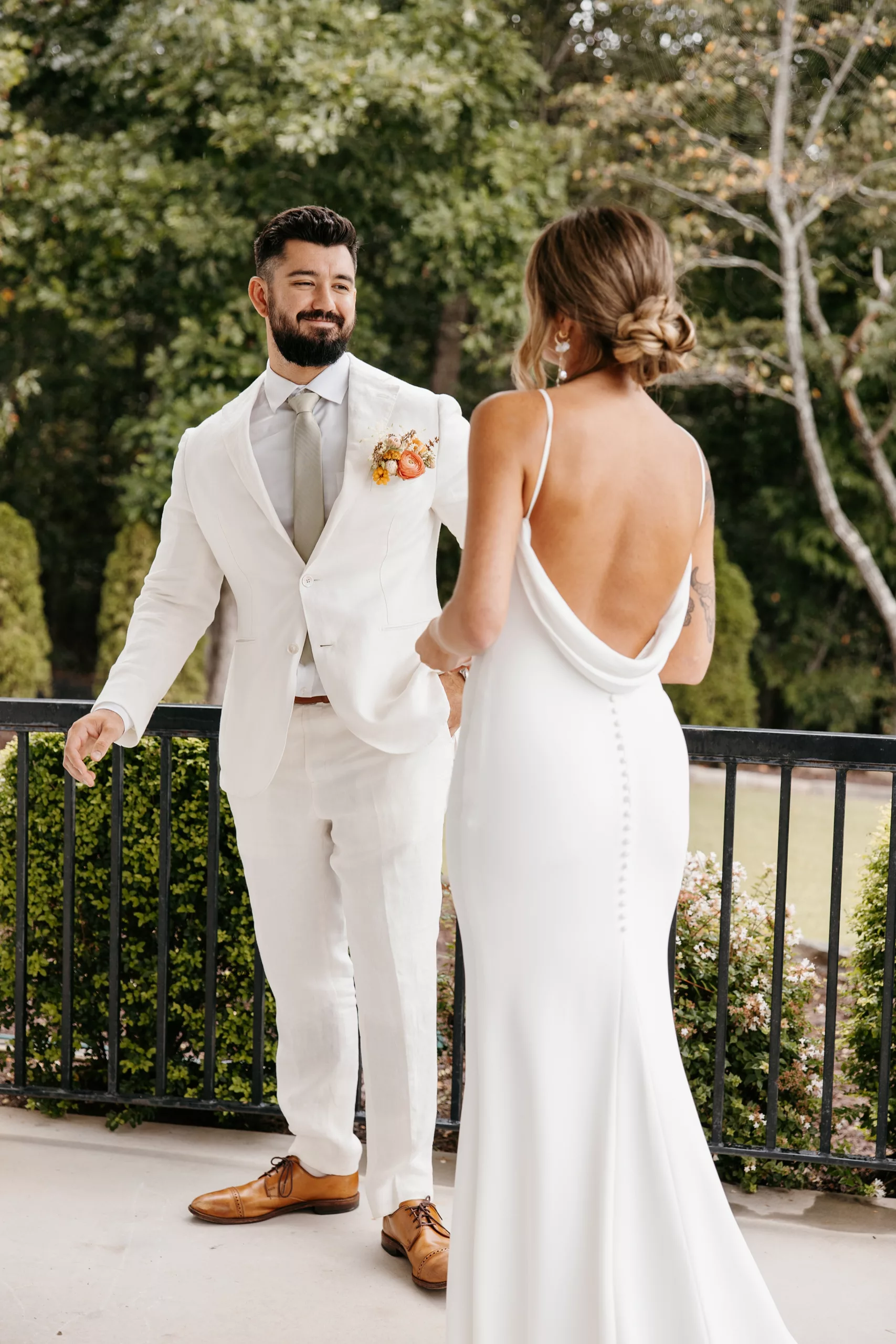 A groom smiles big as he turns around to see his bride for the first time as he wears a white suit