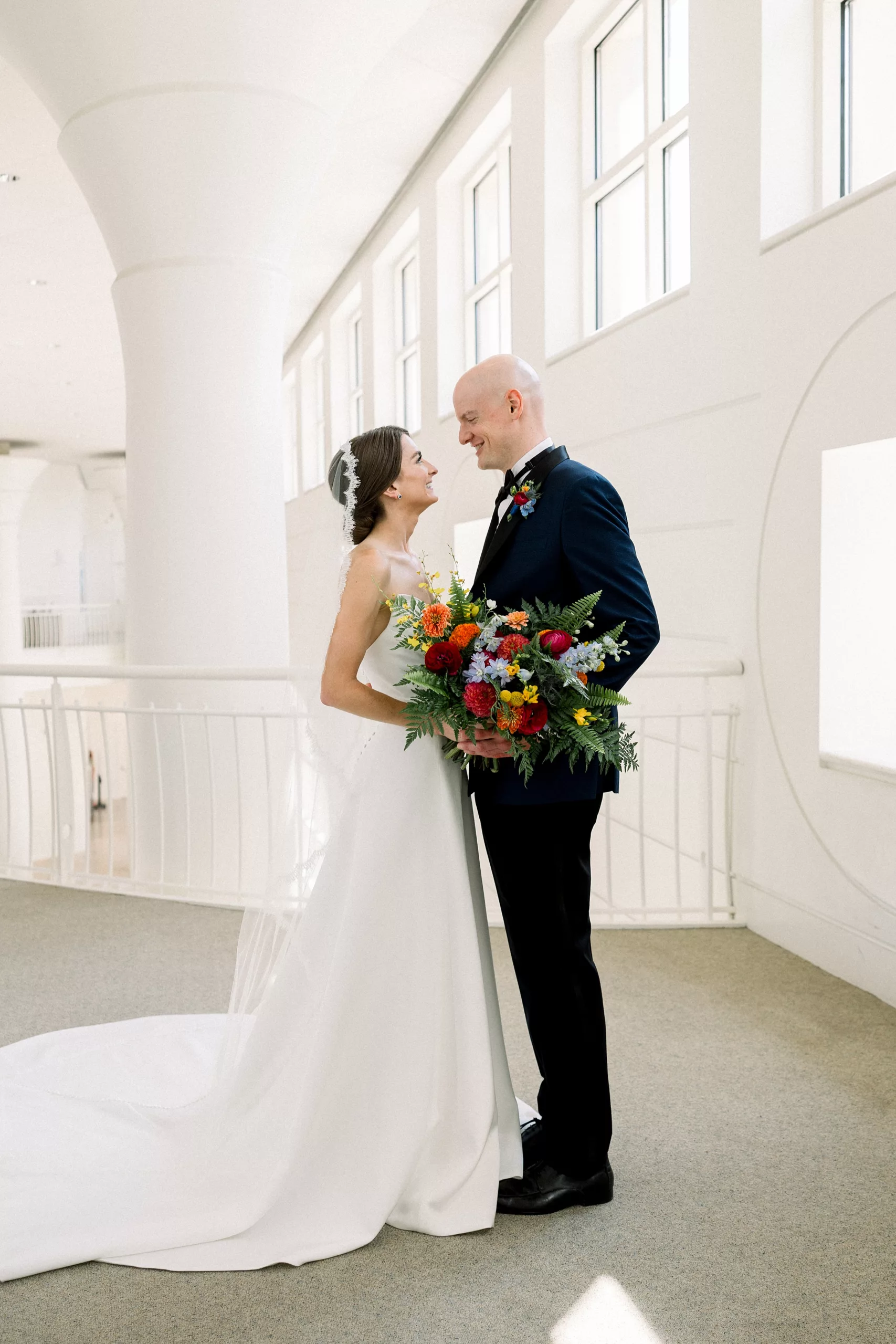 A bride and groom lean in for a kiss while standing in a large white balcony indoors during their first look wedding