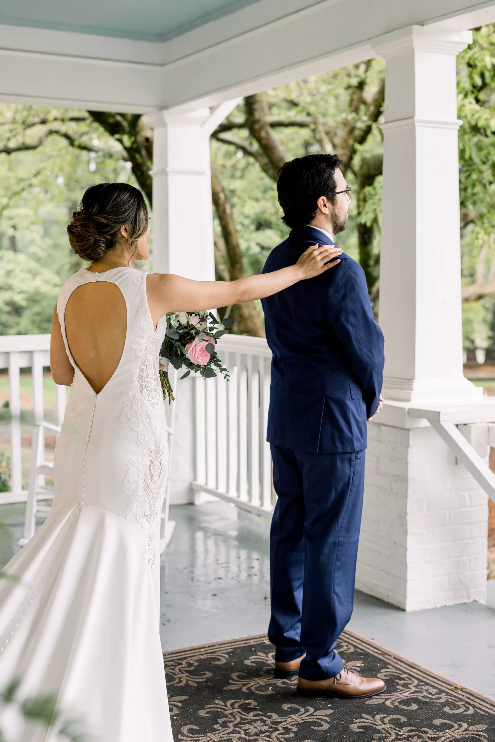 A bride taps the shoulder of her groom in a blue suit so he can turn around for his first look wedding