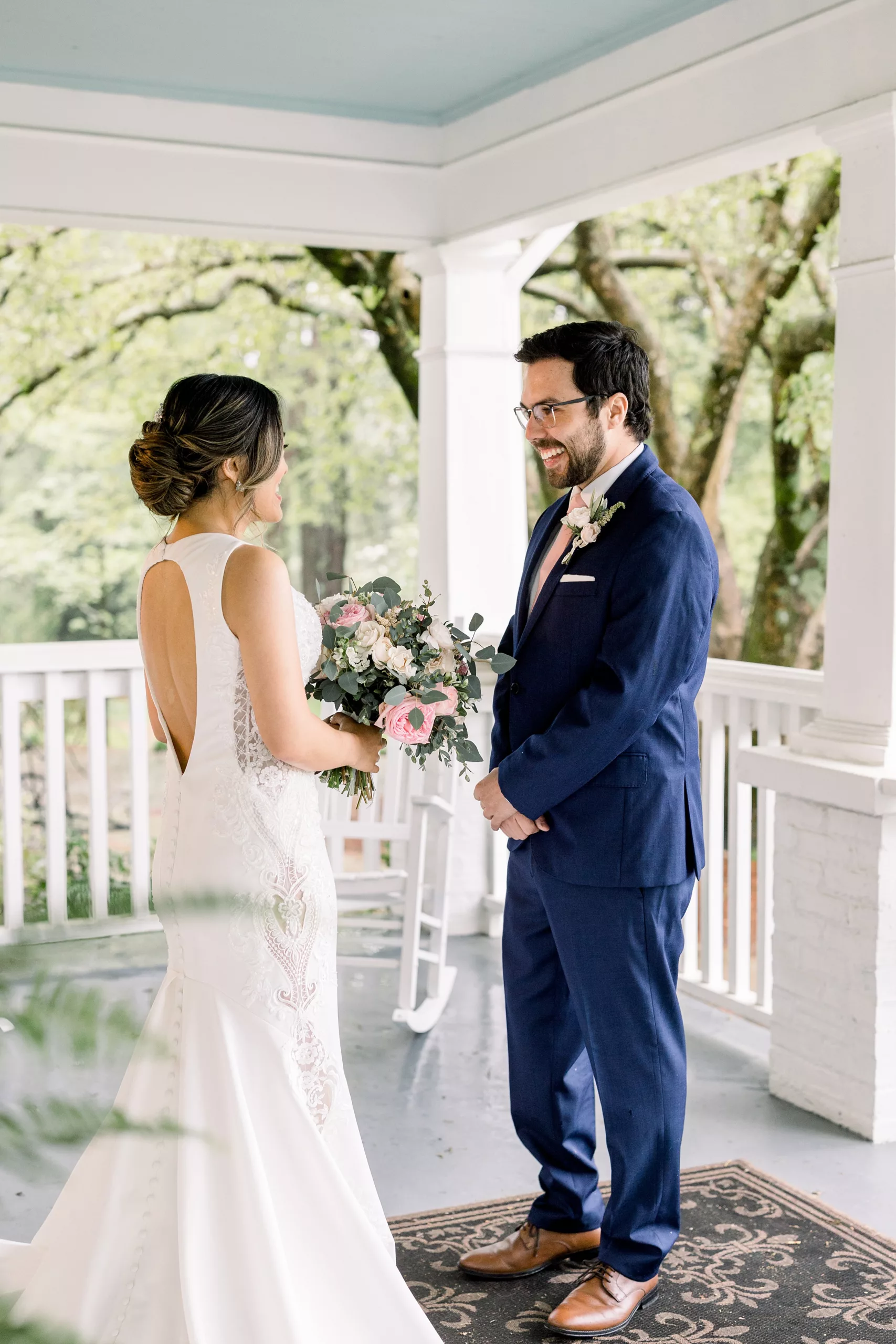 A bride and groom chat and stand together on a porch as he sees her in her dress for the first time during their first look wedding
