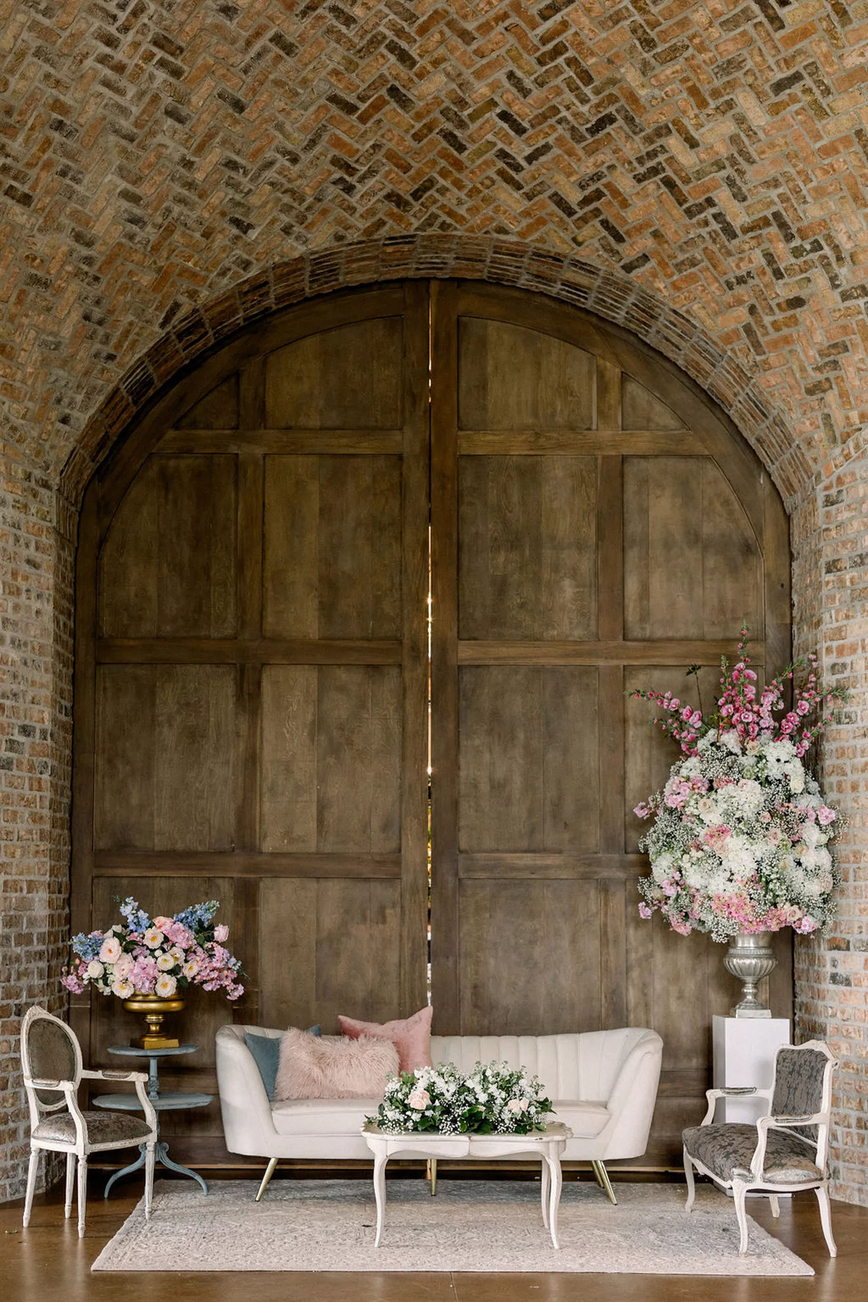 Details of a couch and antique chairs set in a large wooden doorway in a brick room with large floral arrangements at the iron manor wedding venue
