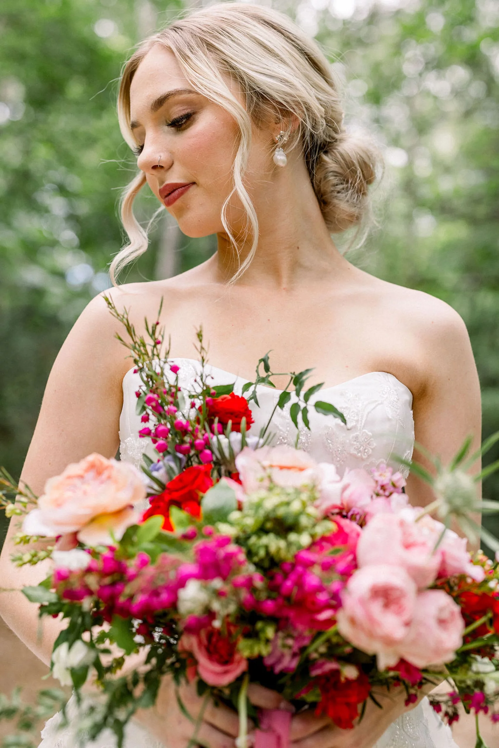 A bride stands in a embroidered dress holding her pink and red bouquet looking down her shoulder at an iron manor wedding