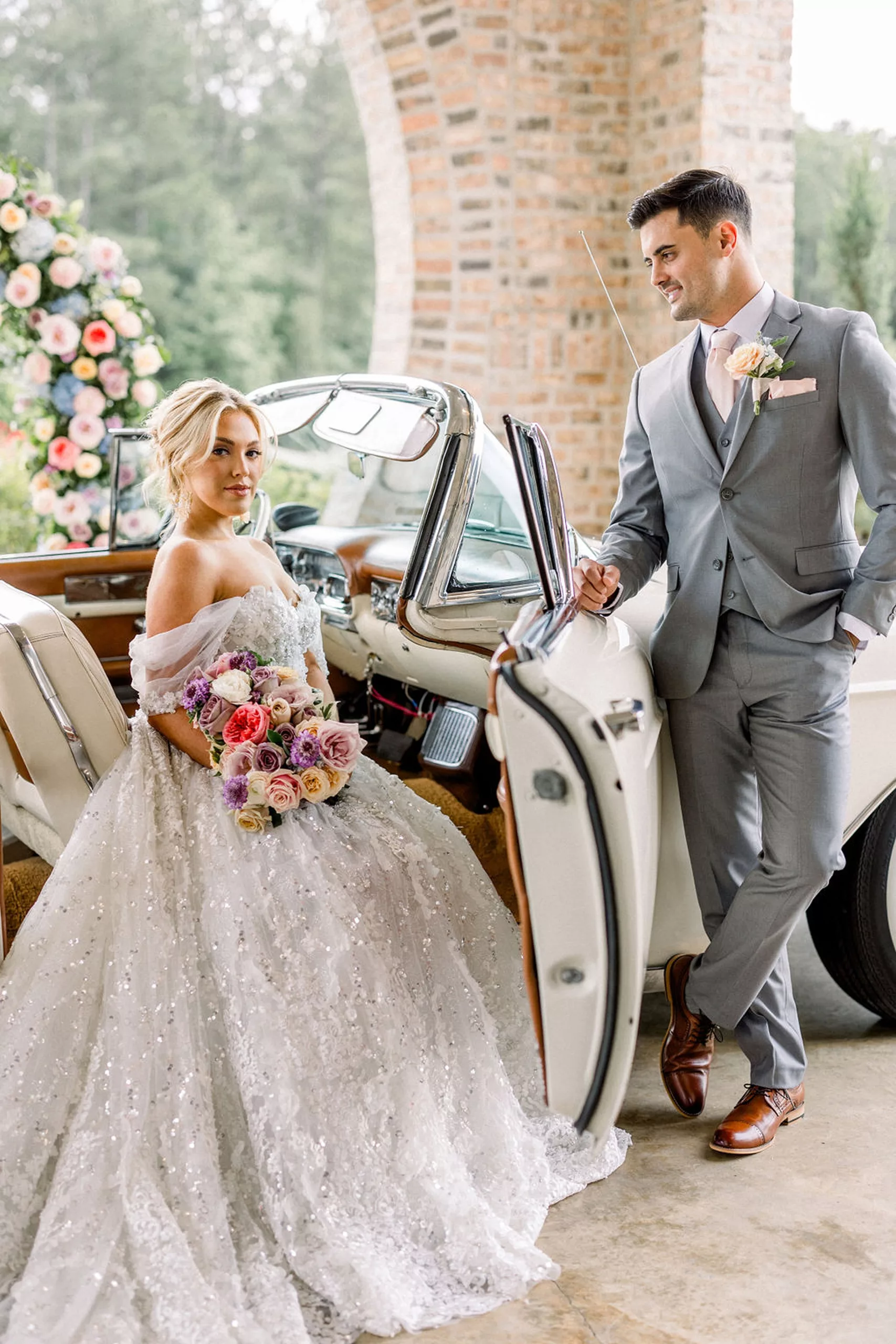 A bride sits in a luxury antique white convertible while her groom leans against the door