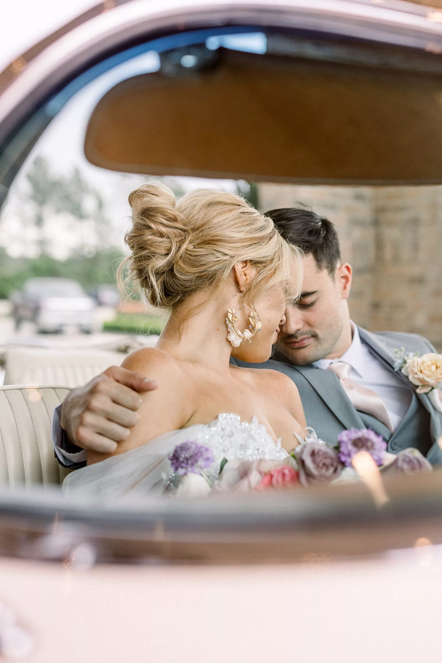 Newlyweds lean in close touching foreheads while sitting in a convertable