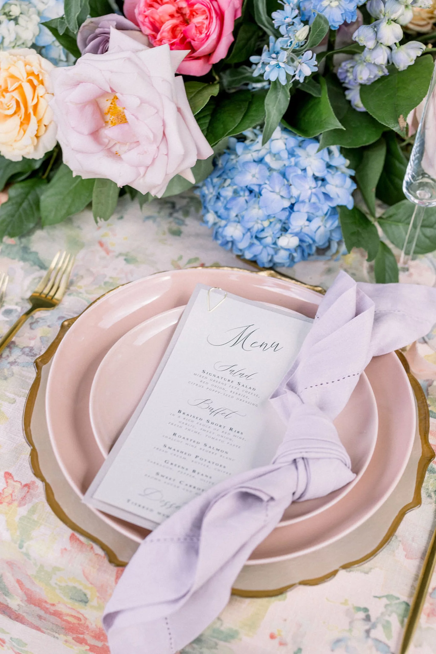 Details of a table setting with pink plate and linen and colorful florals