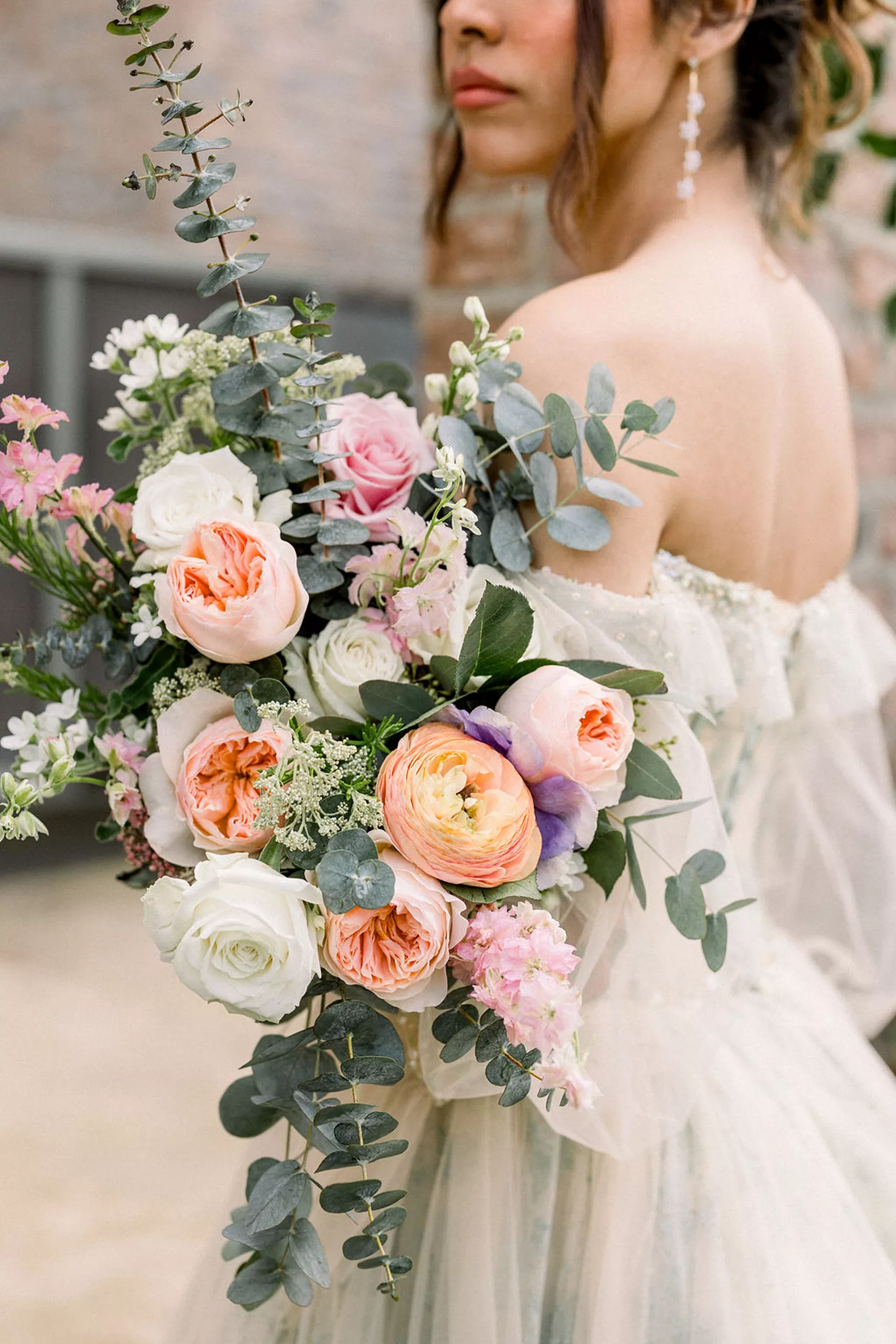A bride stands on a patio holding her large pink and white bouquet