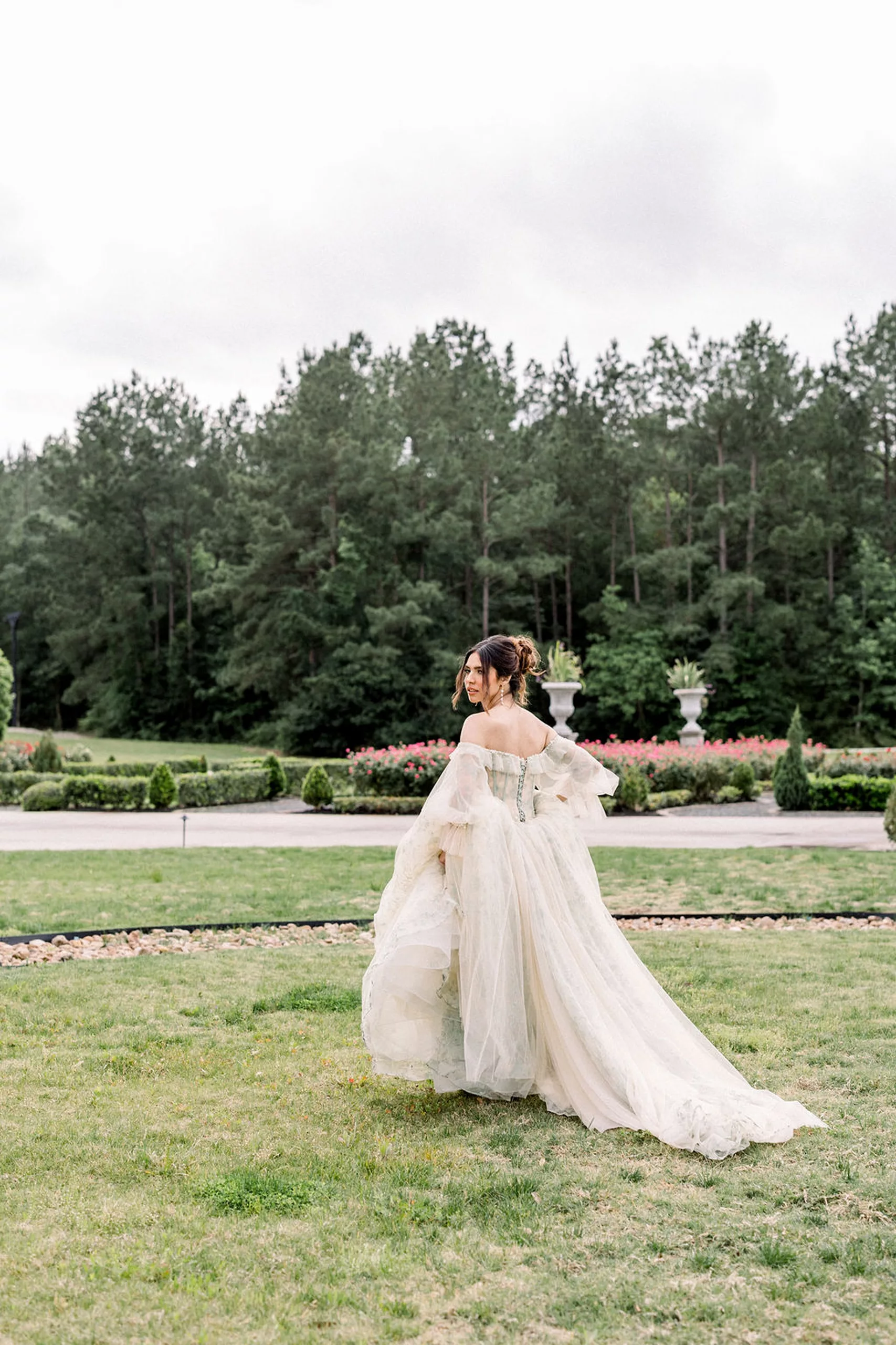 A bride carries her large train while walking through a grassy field in a garden