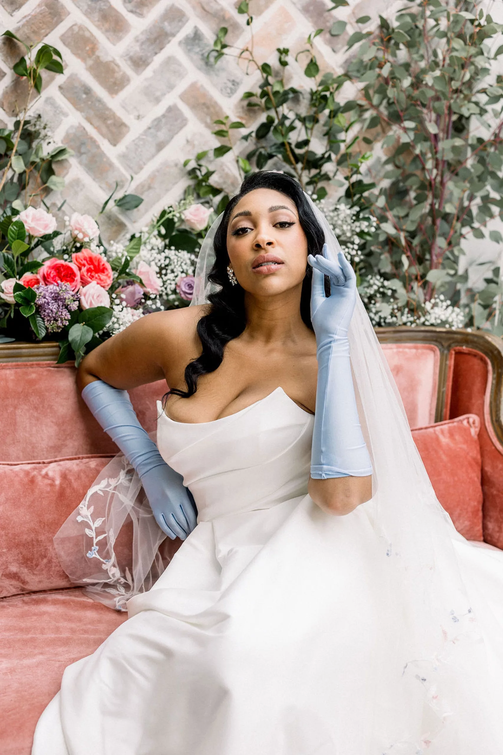 A bride raises her hand in a blue glove as she sits in a pink couch