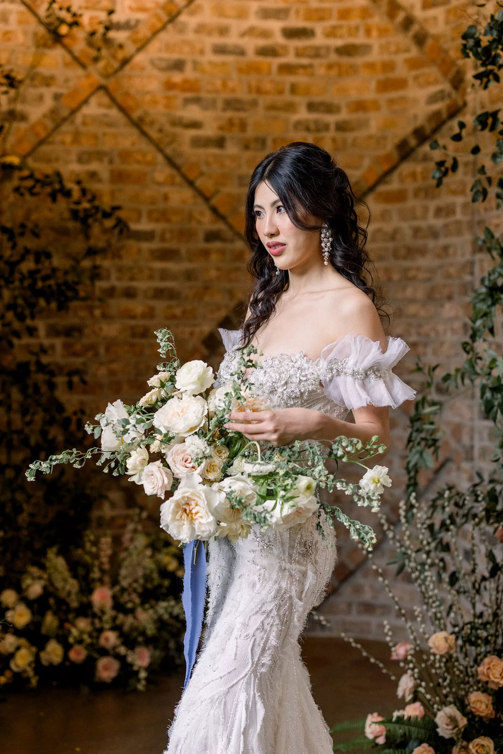 A bride holds her bouquet while standing in a brick room with large white roses