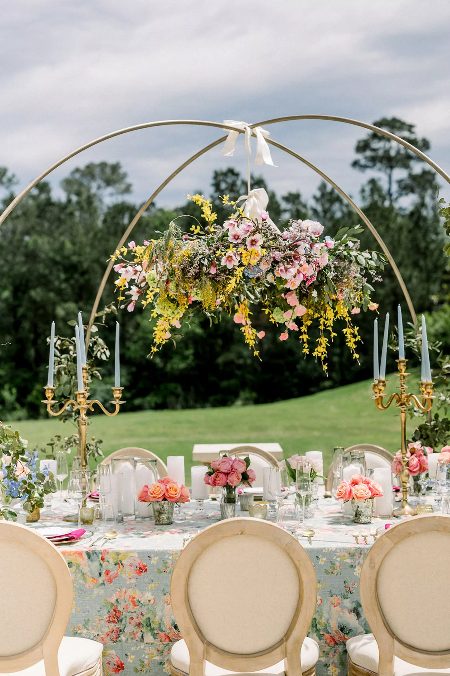 Details of an outdoor reception set up with a gold arch holding a large floating floral centerpiece at an iron manor wedding