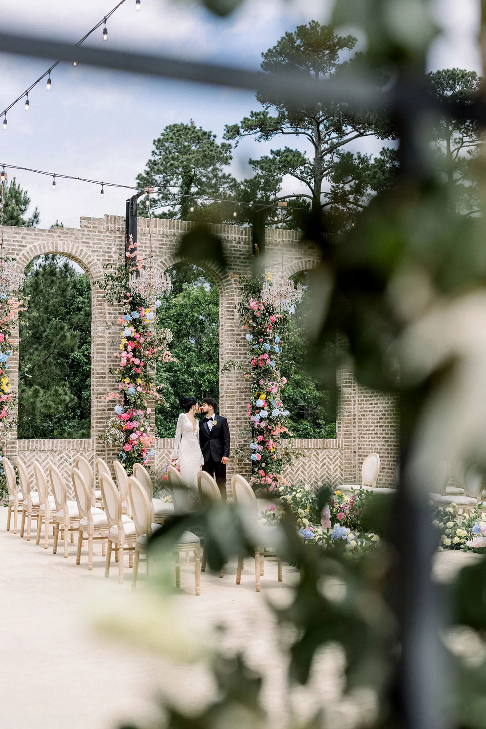 Newlyweds lean in for a kiss under a brick arch in the outdoor wedding ceremony location at iron manor wedding