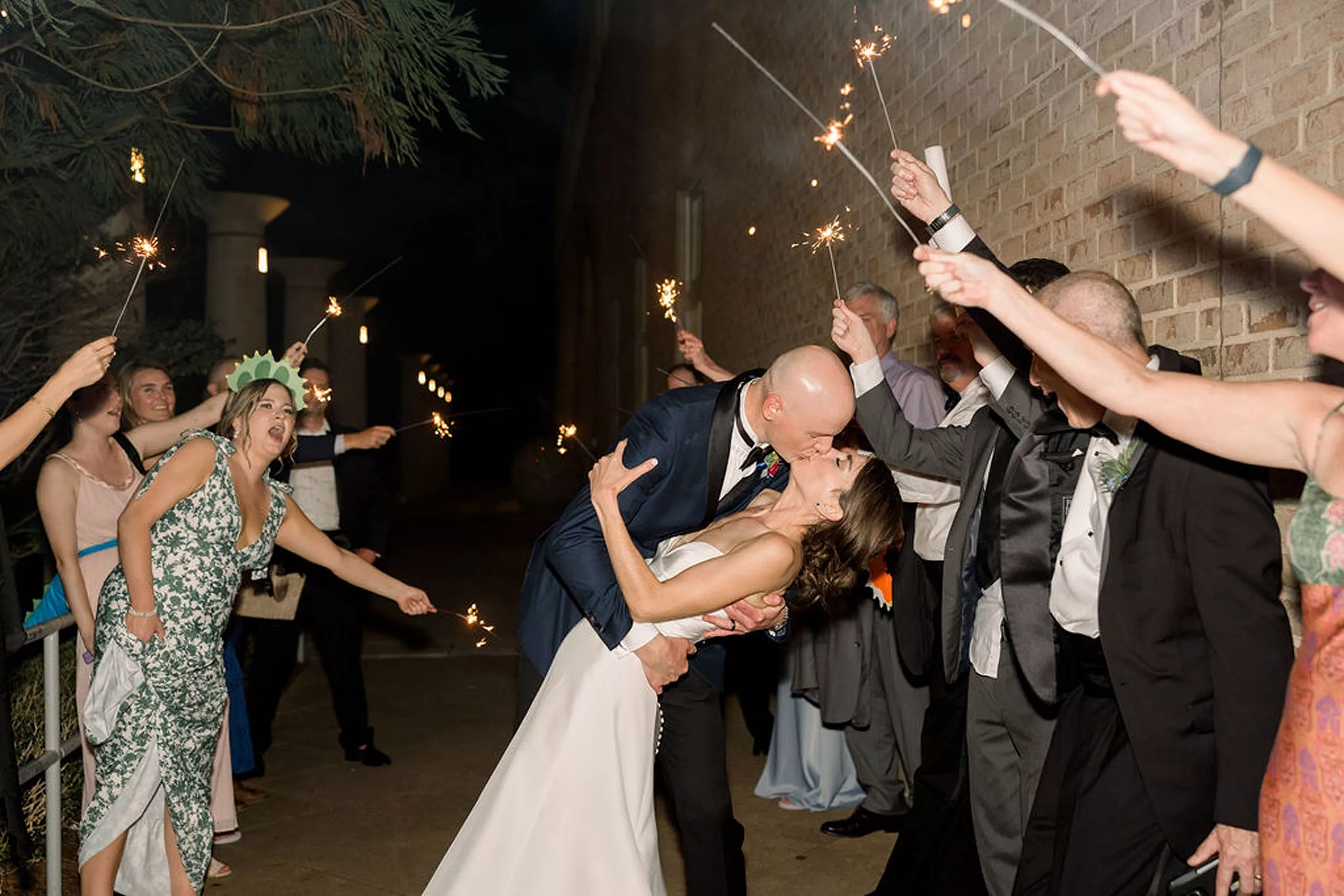 A bride and groom kiss and dip under a shower of sparklers being held by their guests