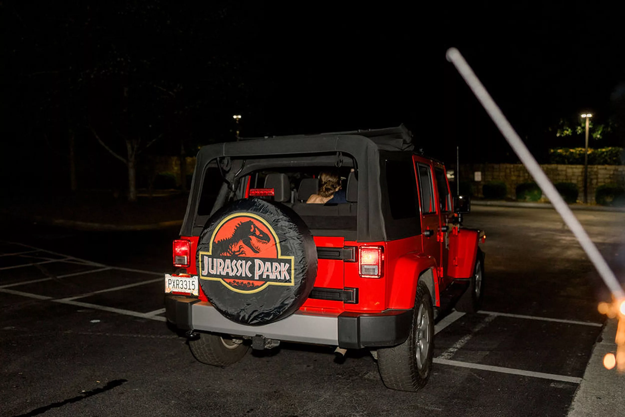 A red Jeep with a Jurassic Park tire cover leaves a wedding with the newlyweds in the back