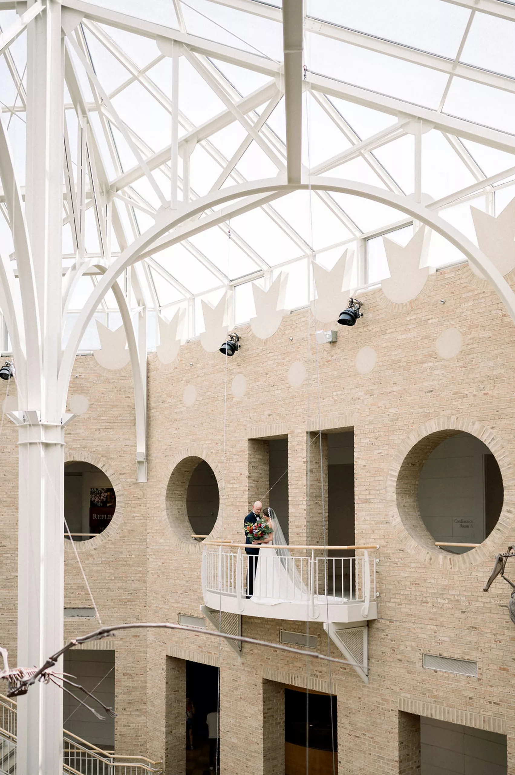 Newlyweds dance alone on a balcony in a museum overlooking dinosaur skeletons