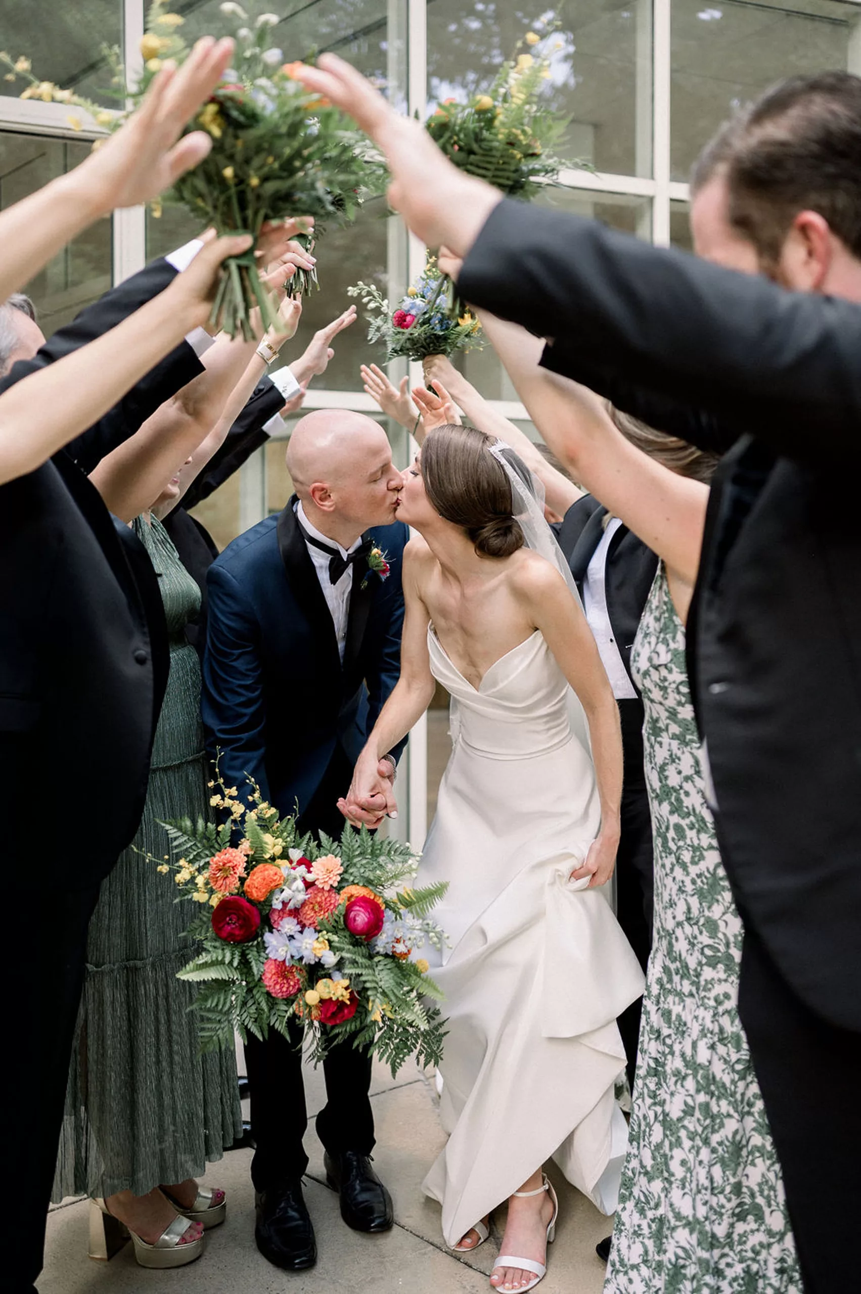 Newlyweds kiss under the hands and bouquets of their guests