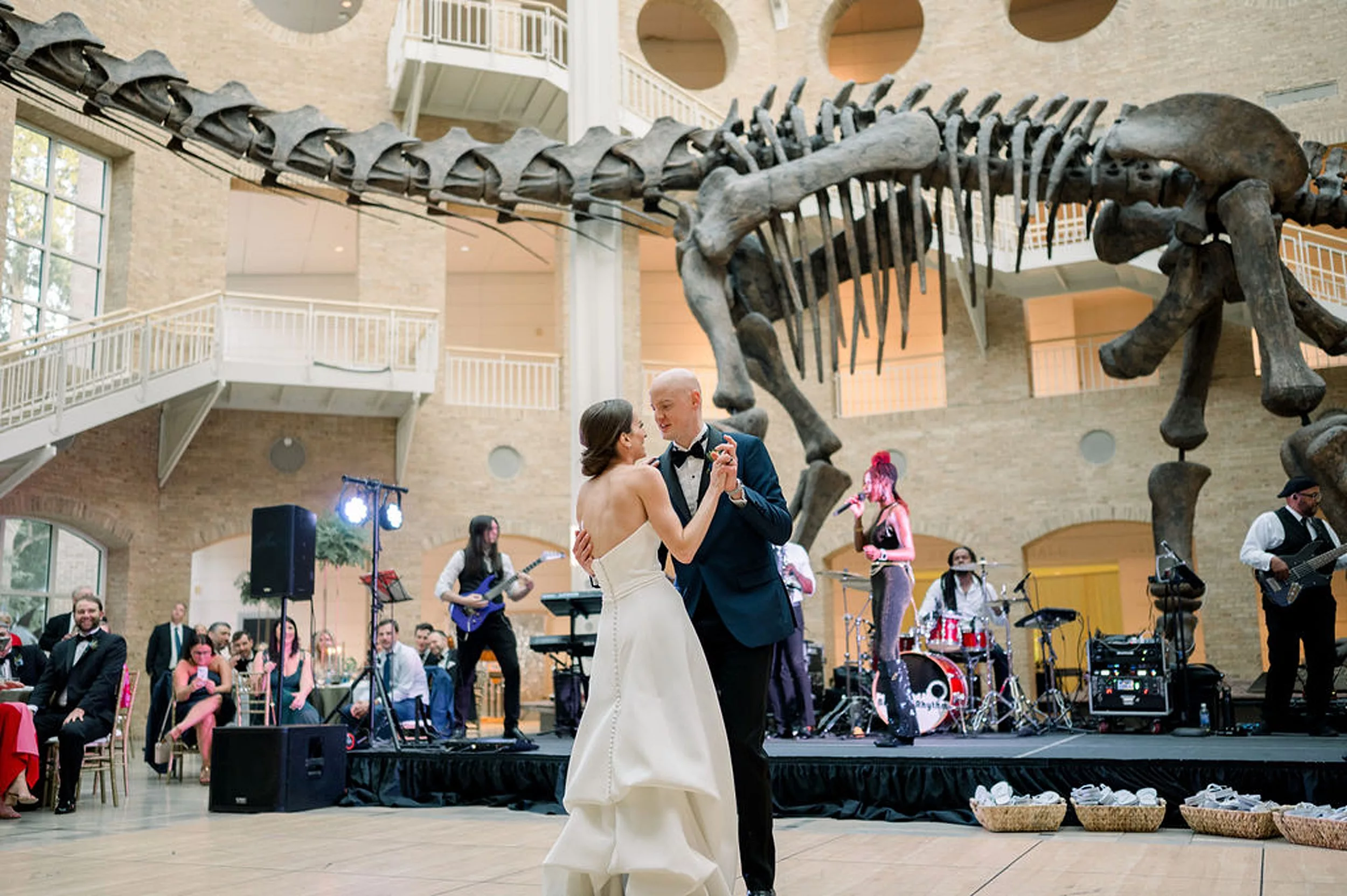 Newlyweds dance as a band plays under a real dinosaur skeleton and their guests look on