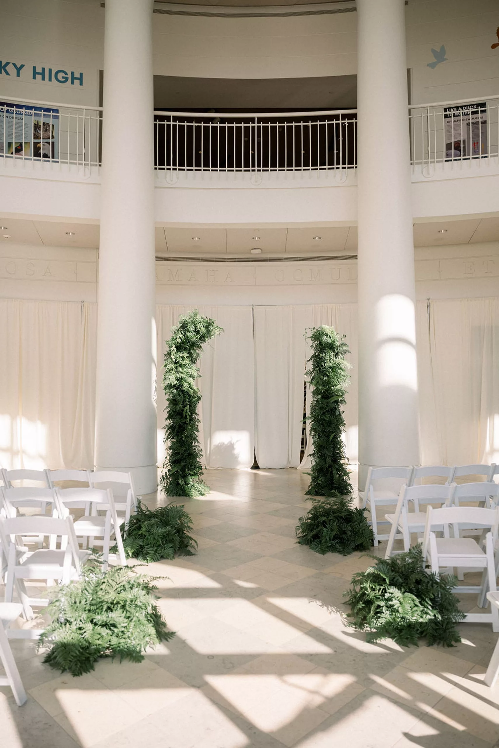 Details of a wedding ceremony setup with white chairs and ferns for decorations