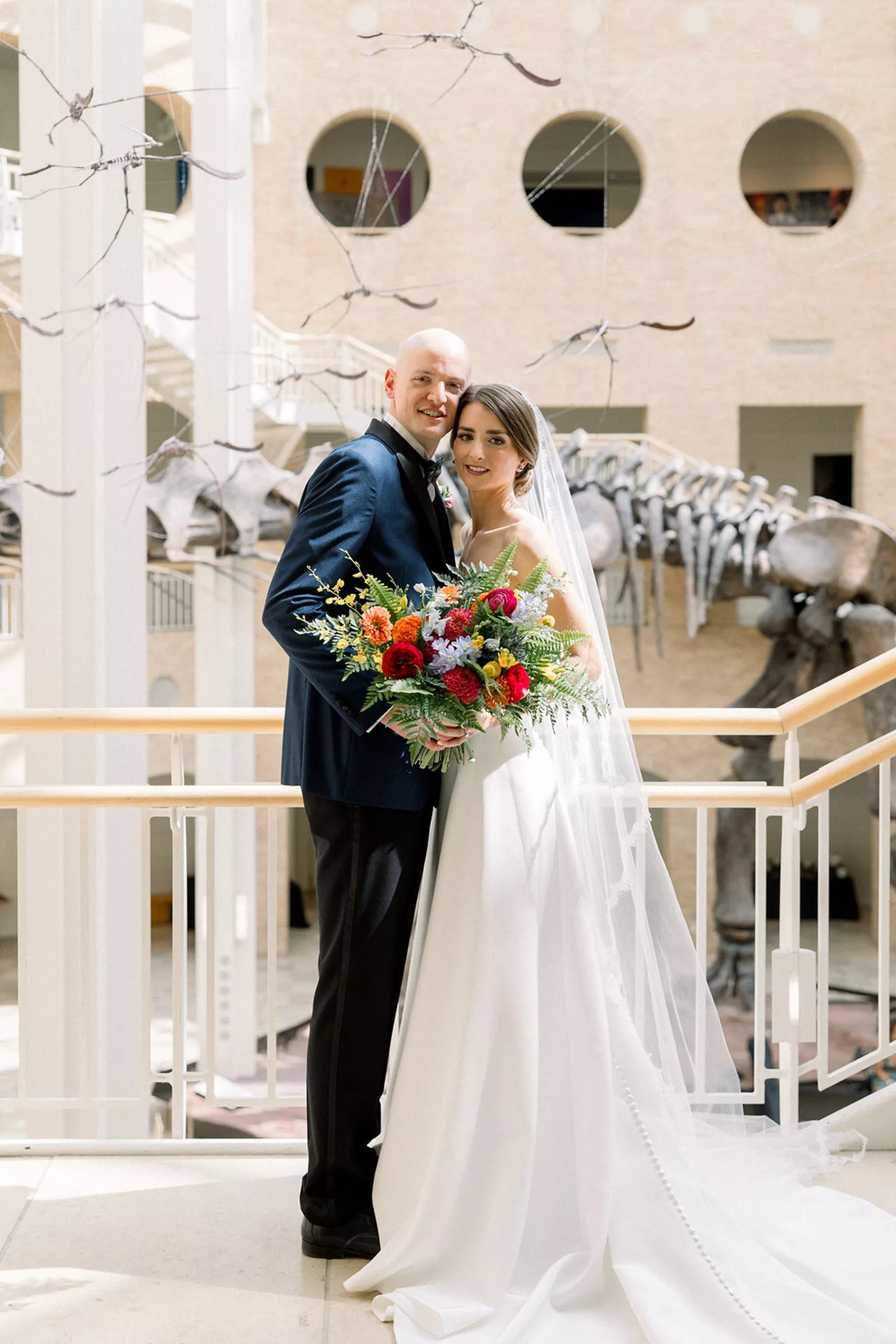Newlyweds stand cheek to cheek under a flock of flying dinosaur skeletons